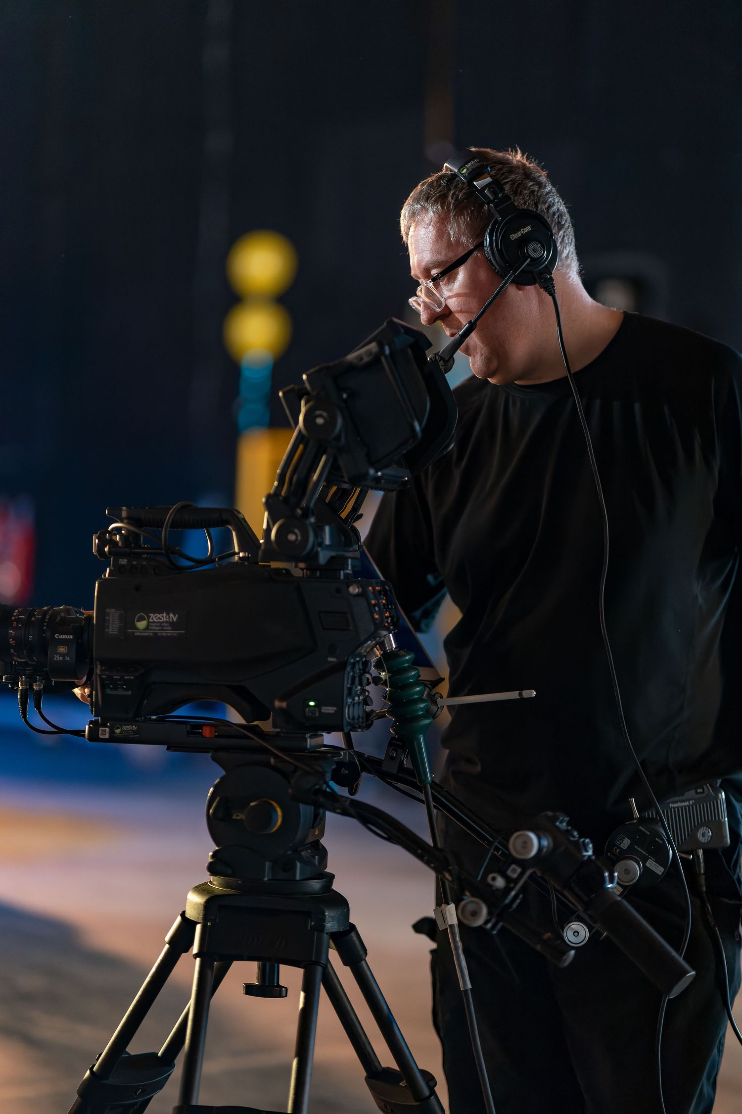 Cameraman with headphones operating a broadcast camera on a tripod in a studio setting, behind the scenes production lifestyle photography