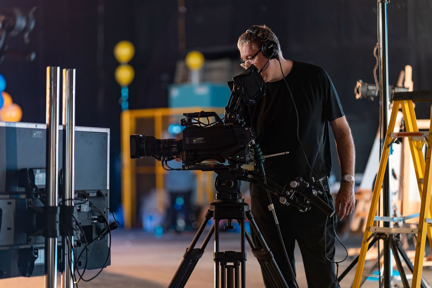 Cameraman operating a broadcast camera on a tripod in a studio setting, behind the scenes production lifestyle photography