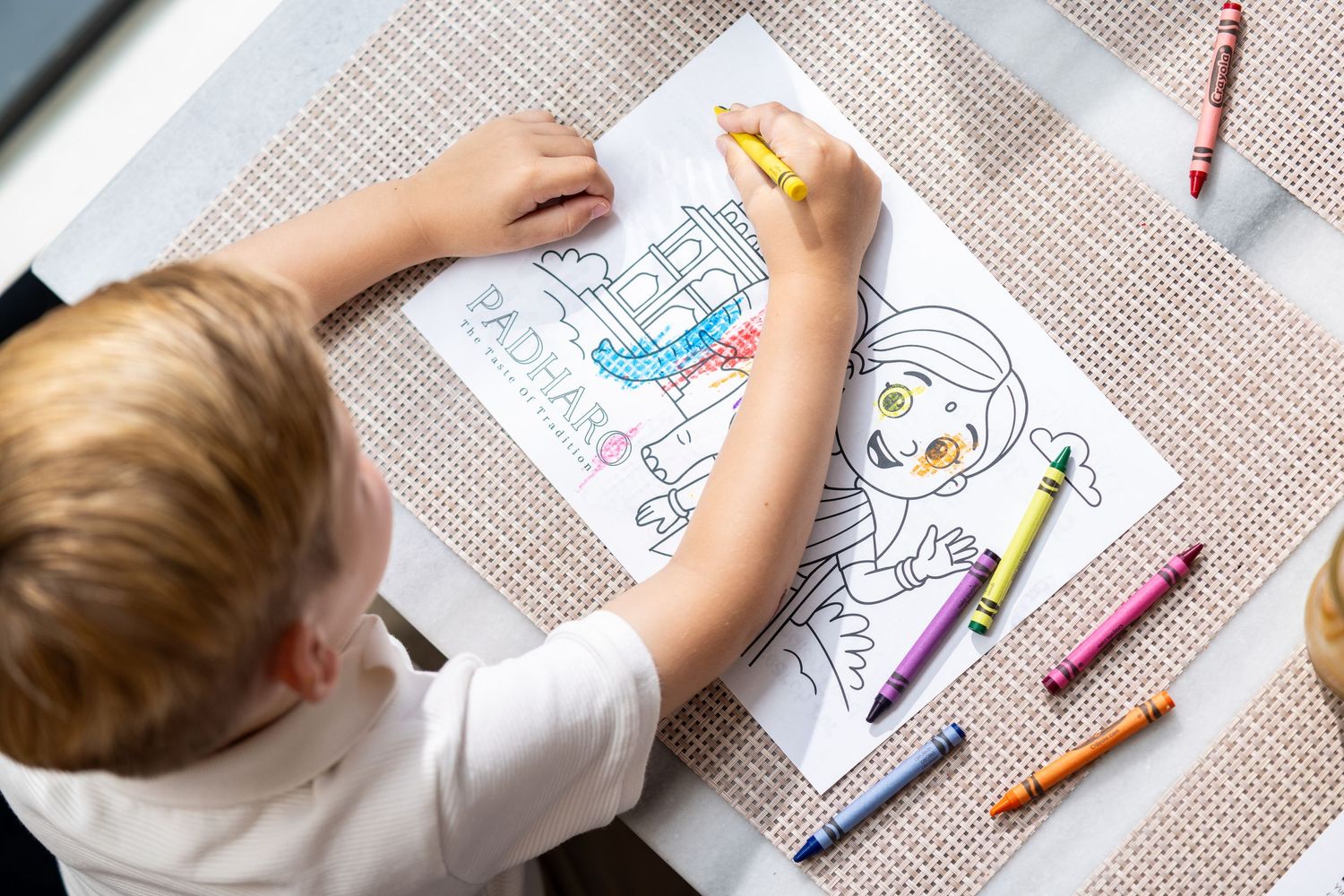 Child colouring in a Padharo activity sheet with crayons at a restaurant table, family dining lifestyle photography Southampton