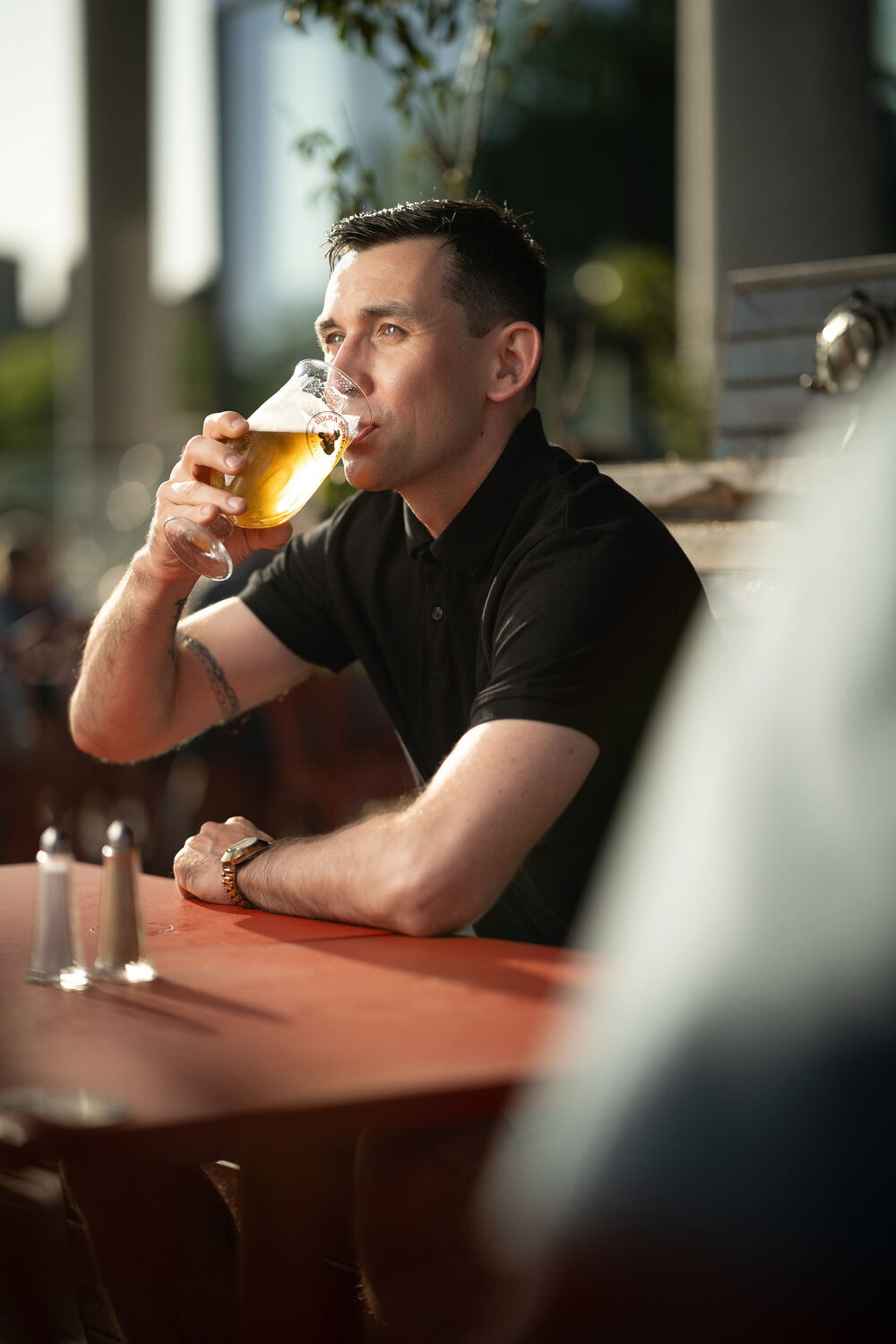 Man in a black polo shirt enjoying a glass of beer at a waterside bar in evening light at Ocean Village, Southampton lifestyle portrait photography