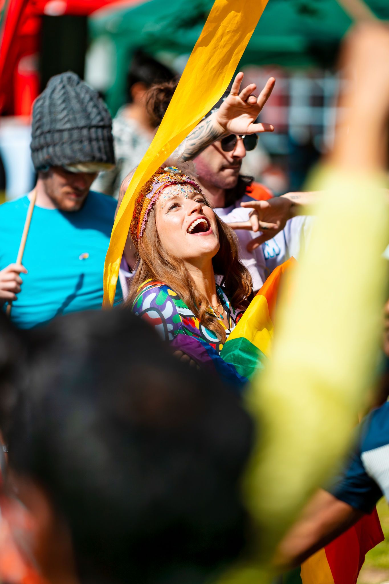 Woman dancing and cheering in the crowd with a glitter headband and rainbow flag at Southampton Pride, colourful festival lifestyle photography