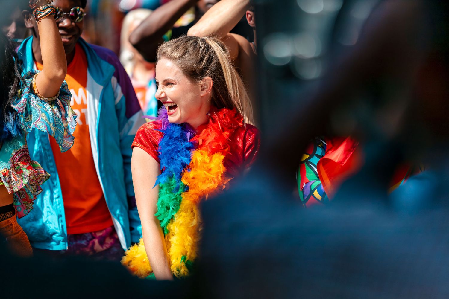 Woman laughing and dancing wearing a rainbow feather boa at Southampton Pride, candid festival lifestyle photography