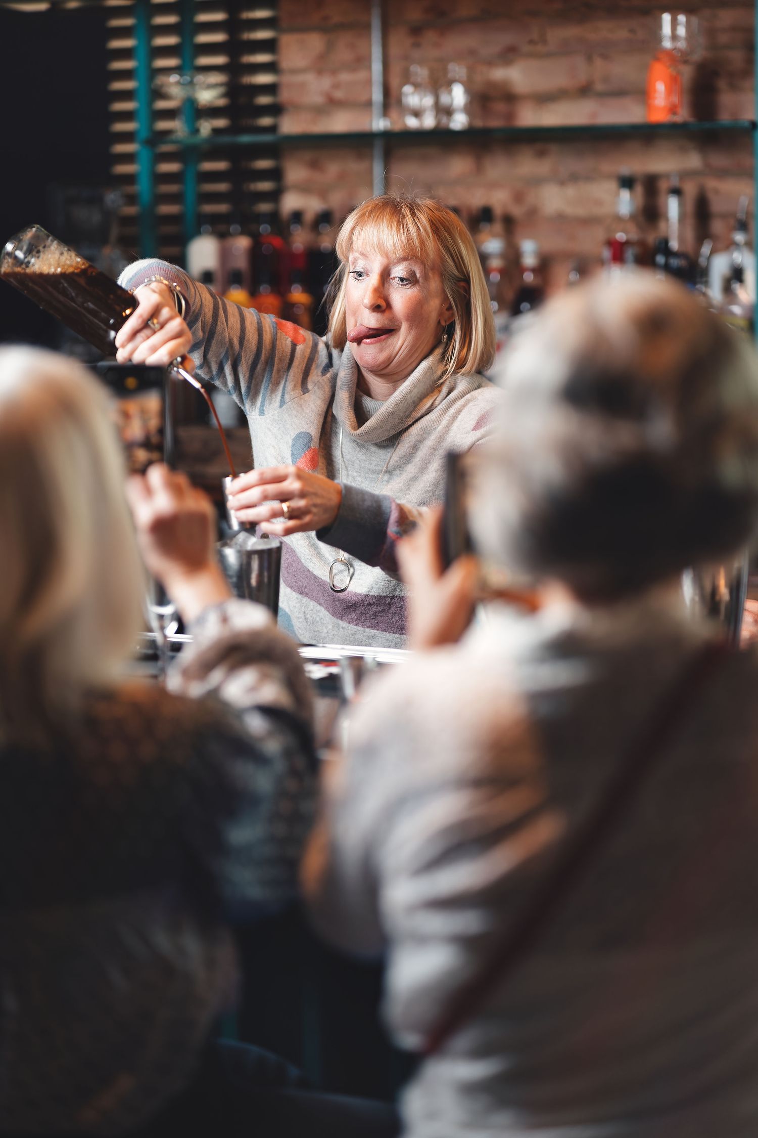 Woman pouring a cocktail at a cocktail-making class with others watching and spirits bottles behind, hospitality experience lifestyle photography Southampton