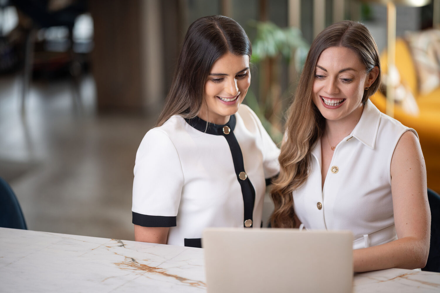 Two colleagues laughing together over a laptop at a marble counter in a bright workspace, team lifestyle photography for Superyacht Crew UK, Southampton