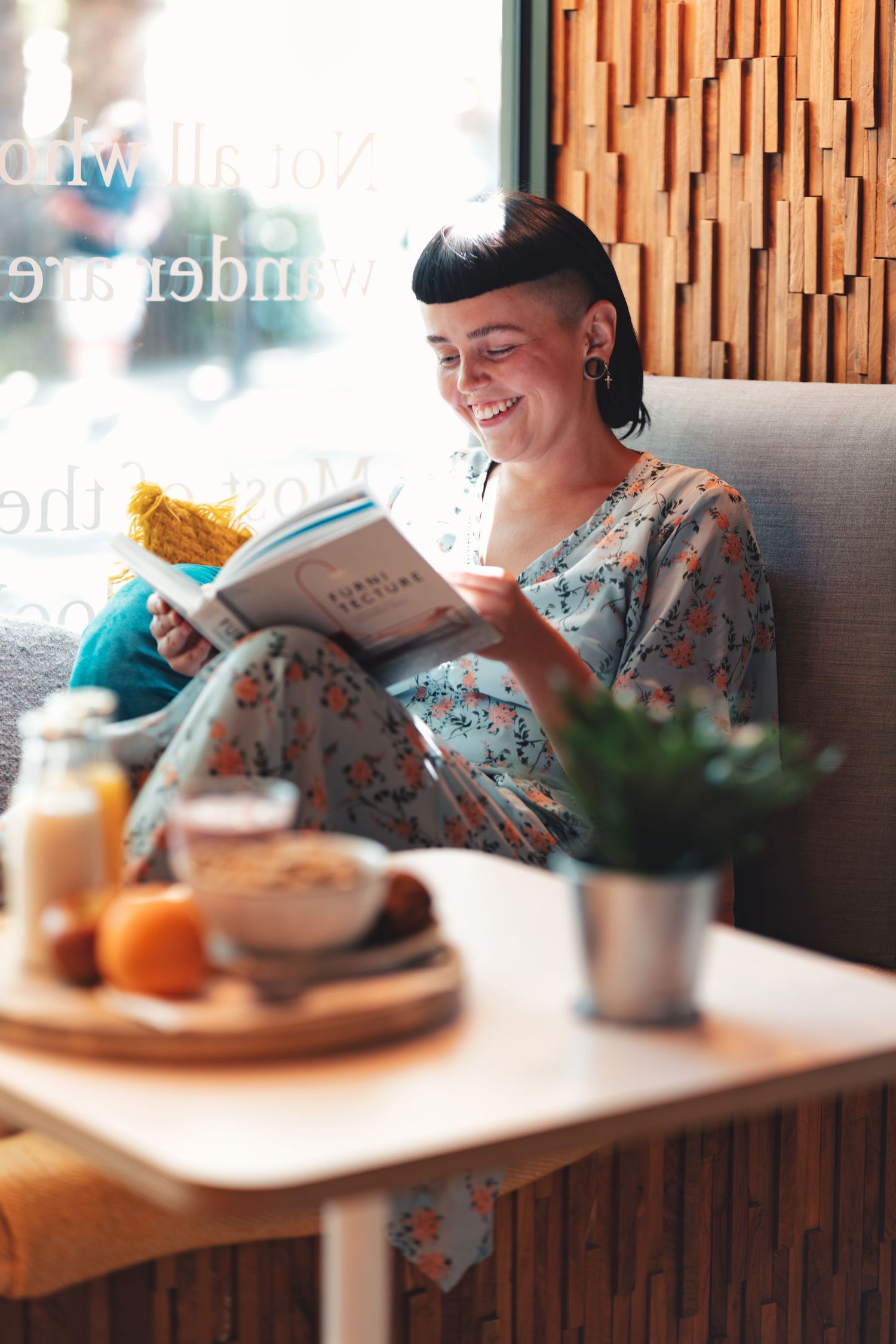 Woman reading a book and smiling by the window with breakfast on the table at a cafe, relaxed cafe lifestyle photography Southampton