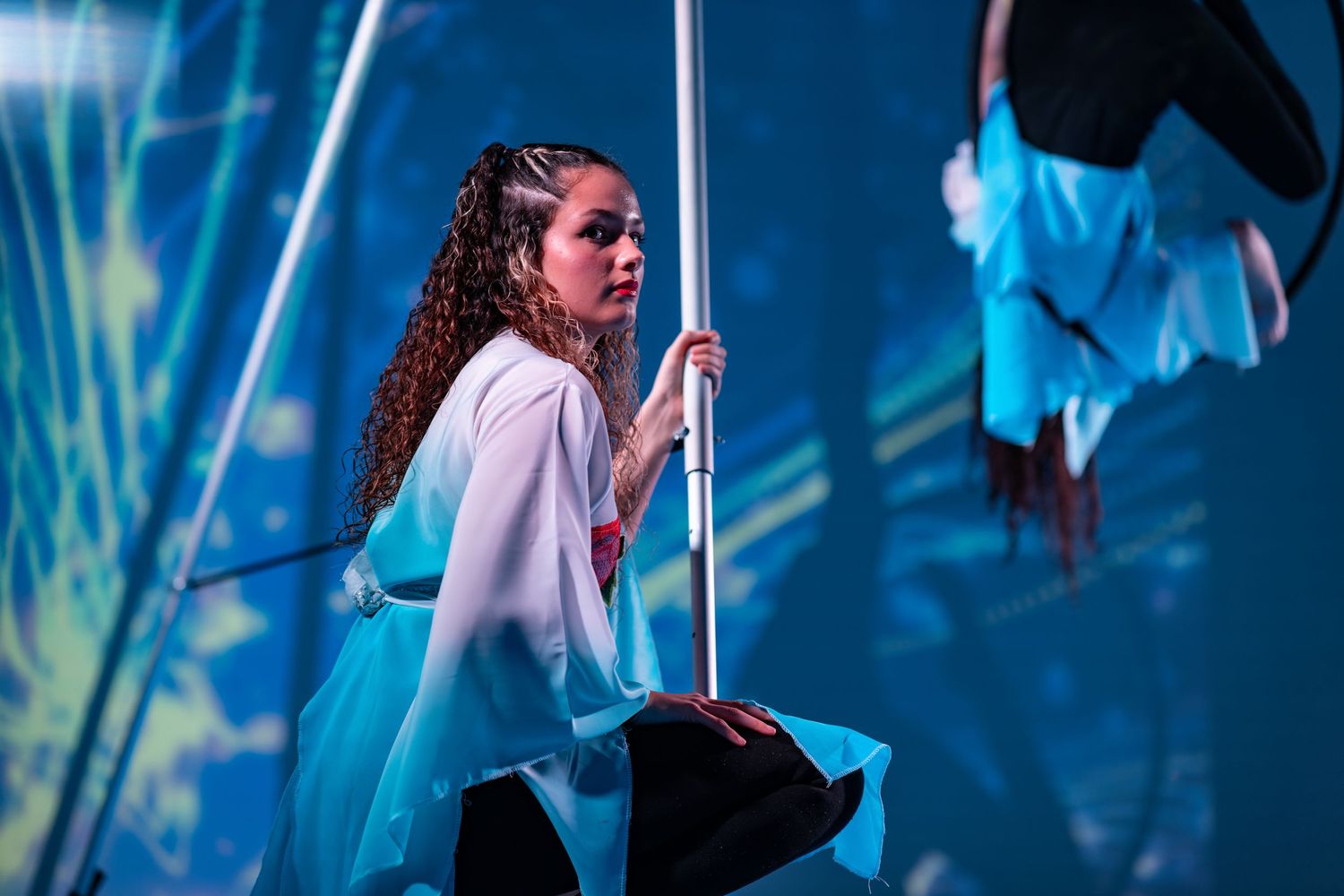 Dancer in a flowing blue and white costume holding a pole on stage with blue lighting and projected backdrop, live performance event photography Southampton