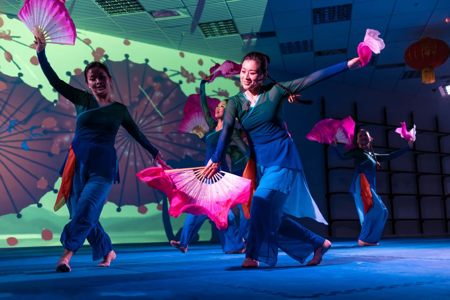 Traditional Chinese fan dancers performing in blue costumes with pink fans and a projected floral backdrop, live cultural event photography Southampton