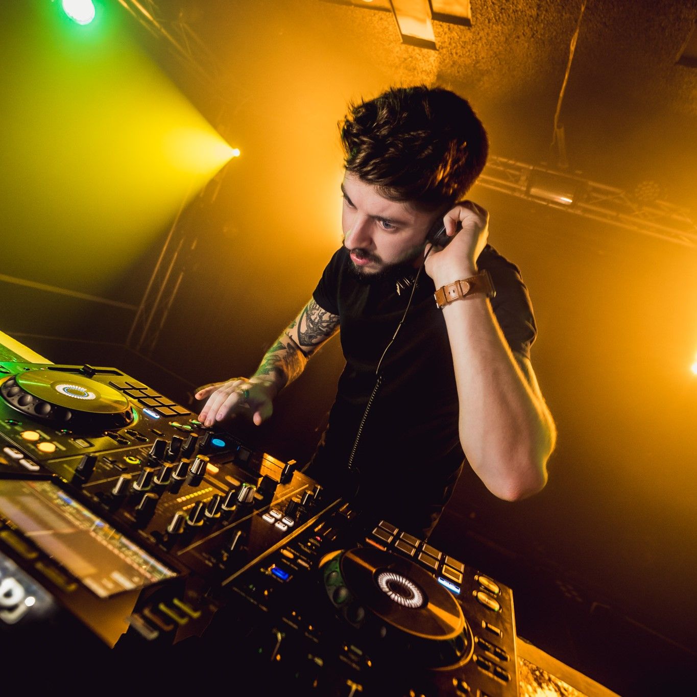 DJ with tattoos mixing at CDJs with amber and yellow stage lighting, nightclub live event photography Southampton