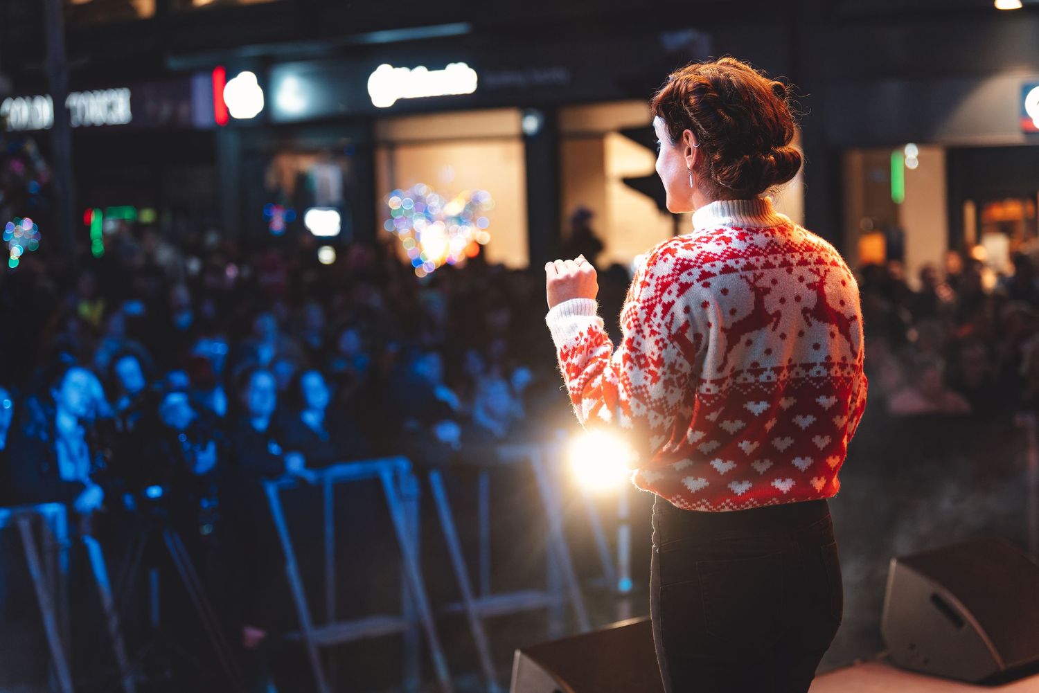 Performer in a Christmas jumper seen from behind on an outdoor stage facing a crowd at a Countdown to Christmas event, live event photography Southampton