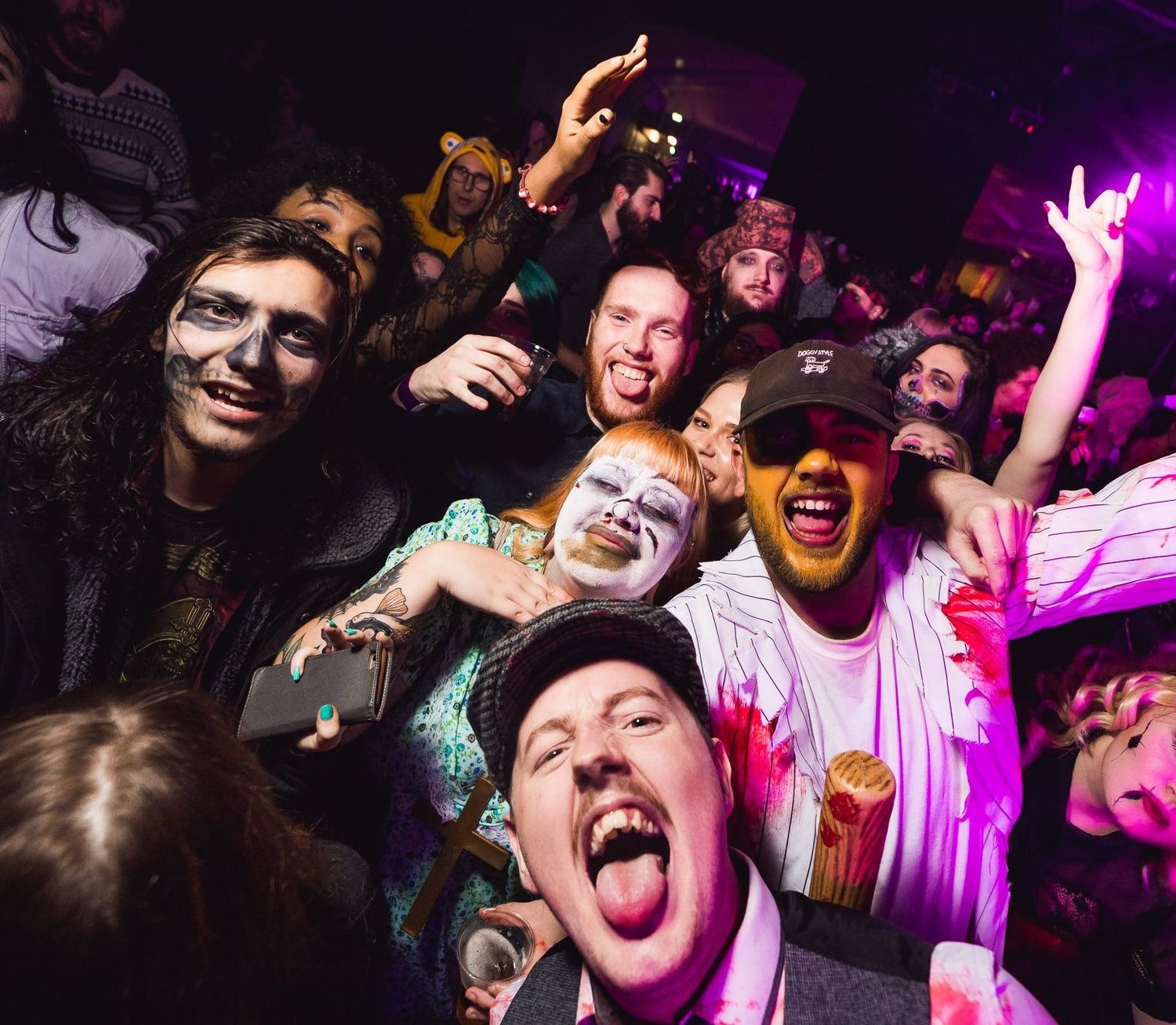 Group of friends in Halloween costumes and face paint cheering at a nightclub party with purple lighting, nightlife event photography Southampton