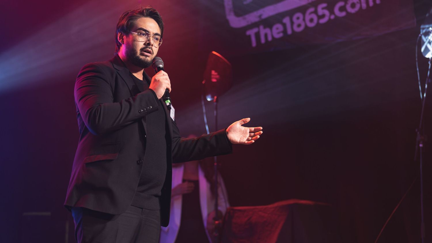 Comedian speaking into a microphone on stage at The 1865 venue Southampton with dramatic red lighting, live event photography