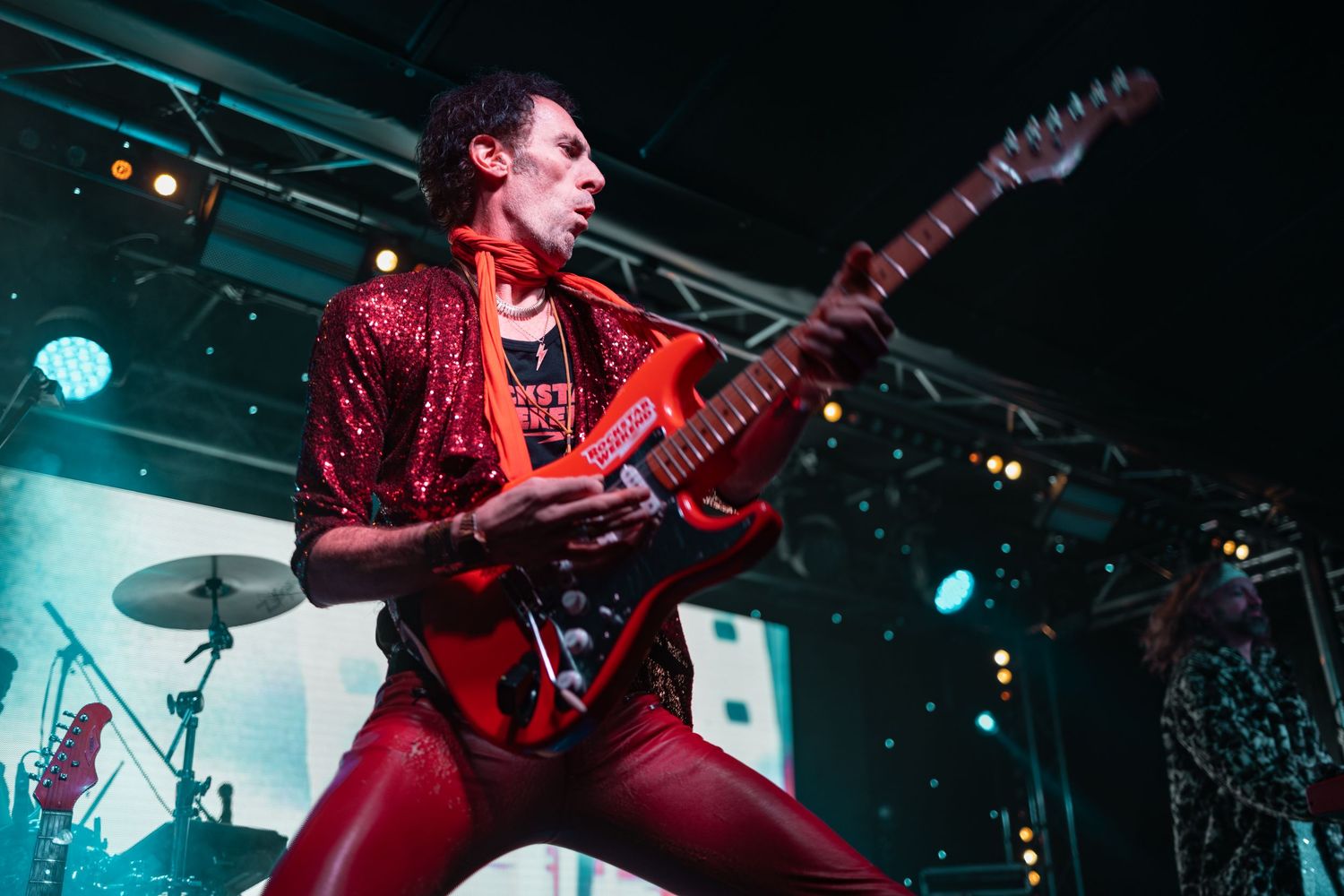 Guitarist in red sequin jacket playing red electric guitar on stage with teal lighting at Countdown to Christmas, live music event photography Southampton