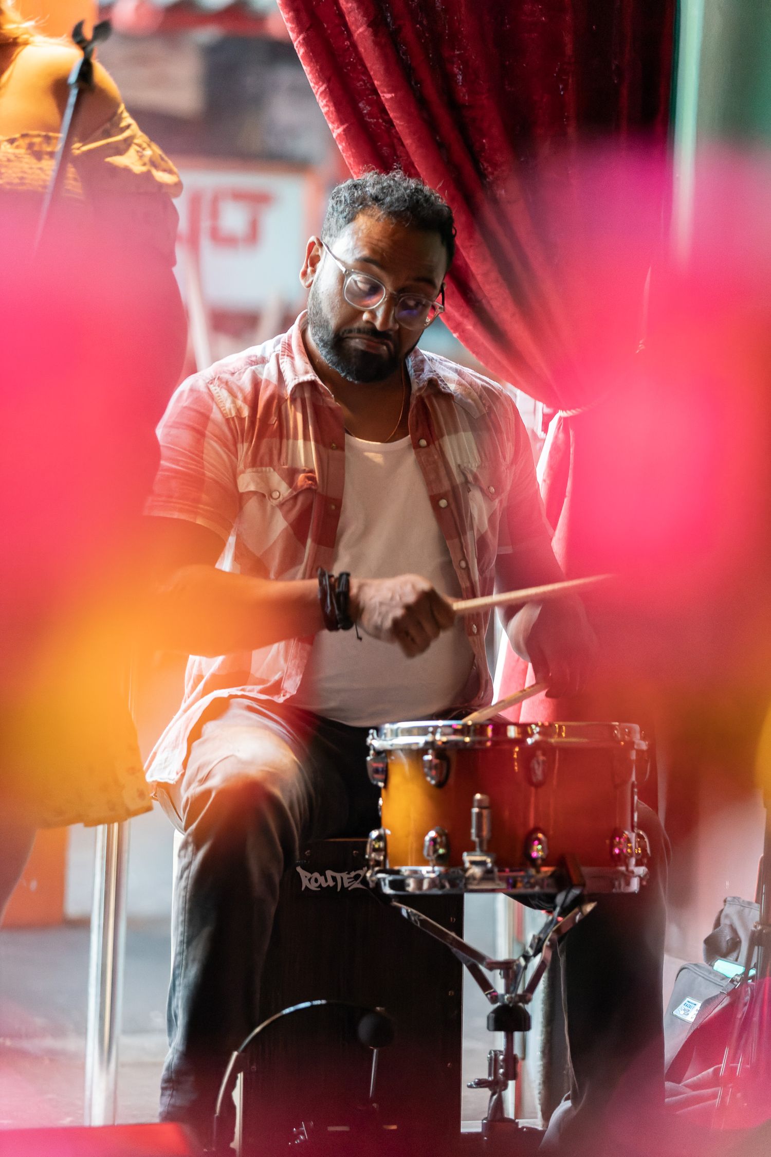 Drummer playing a snare drum at Crib Sessions with warm pink and red light bokeh in the foreground, live music event photography Southampton
