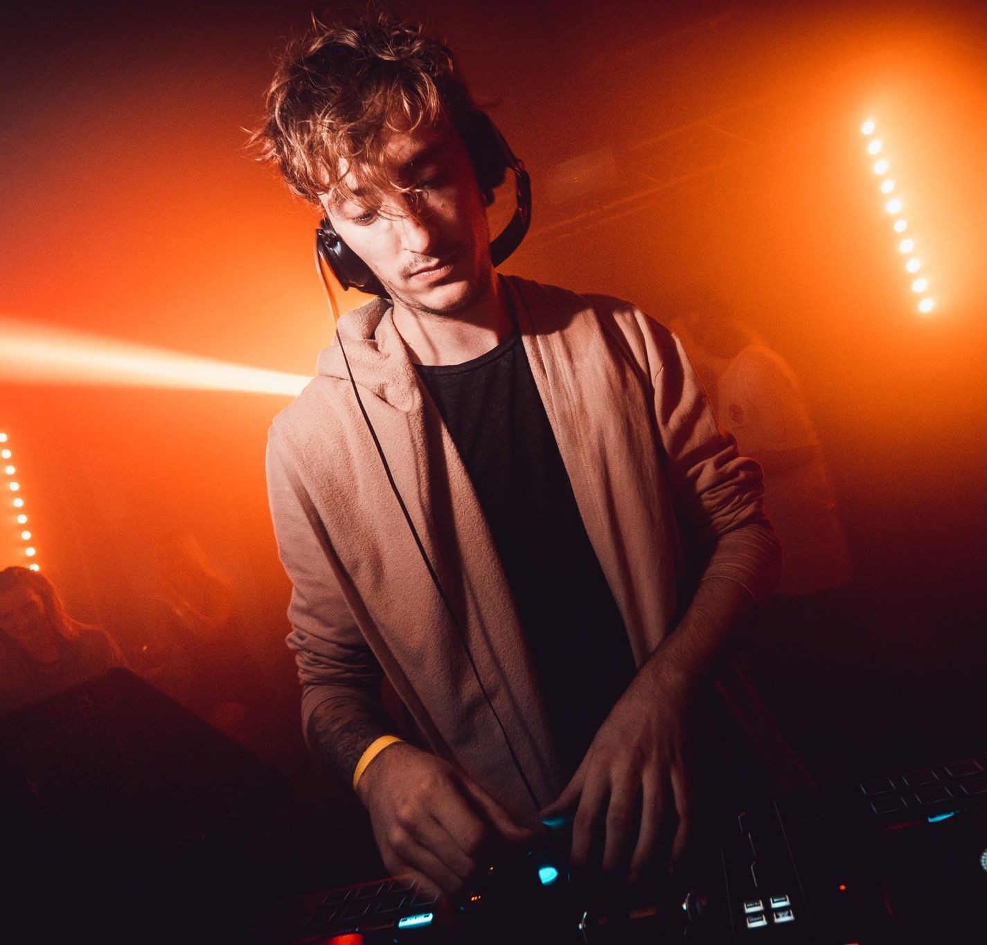 DJ wearing headphones mixing at decks with dramatic orange stage lighting at District, nightclub event photography Southampton