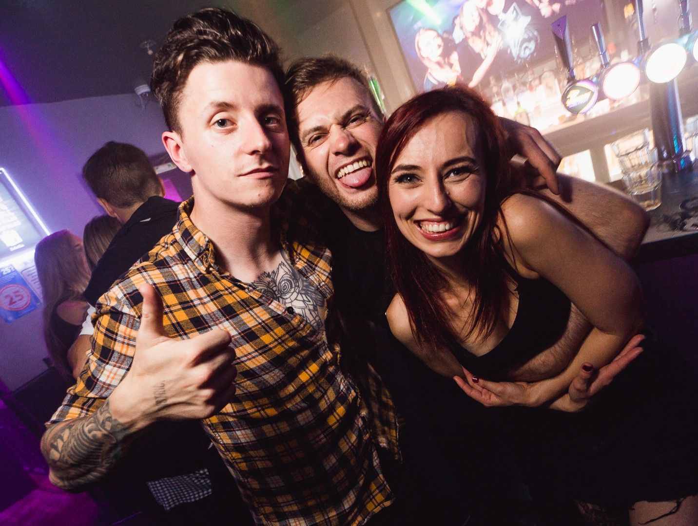 Three friends posing together at a bar with purple nightclub lighting, nightlife event photography Southampton