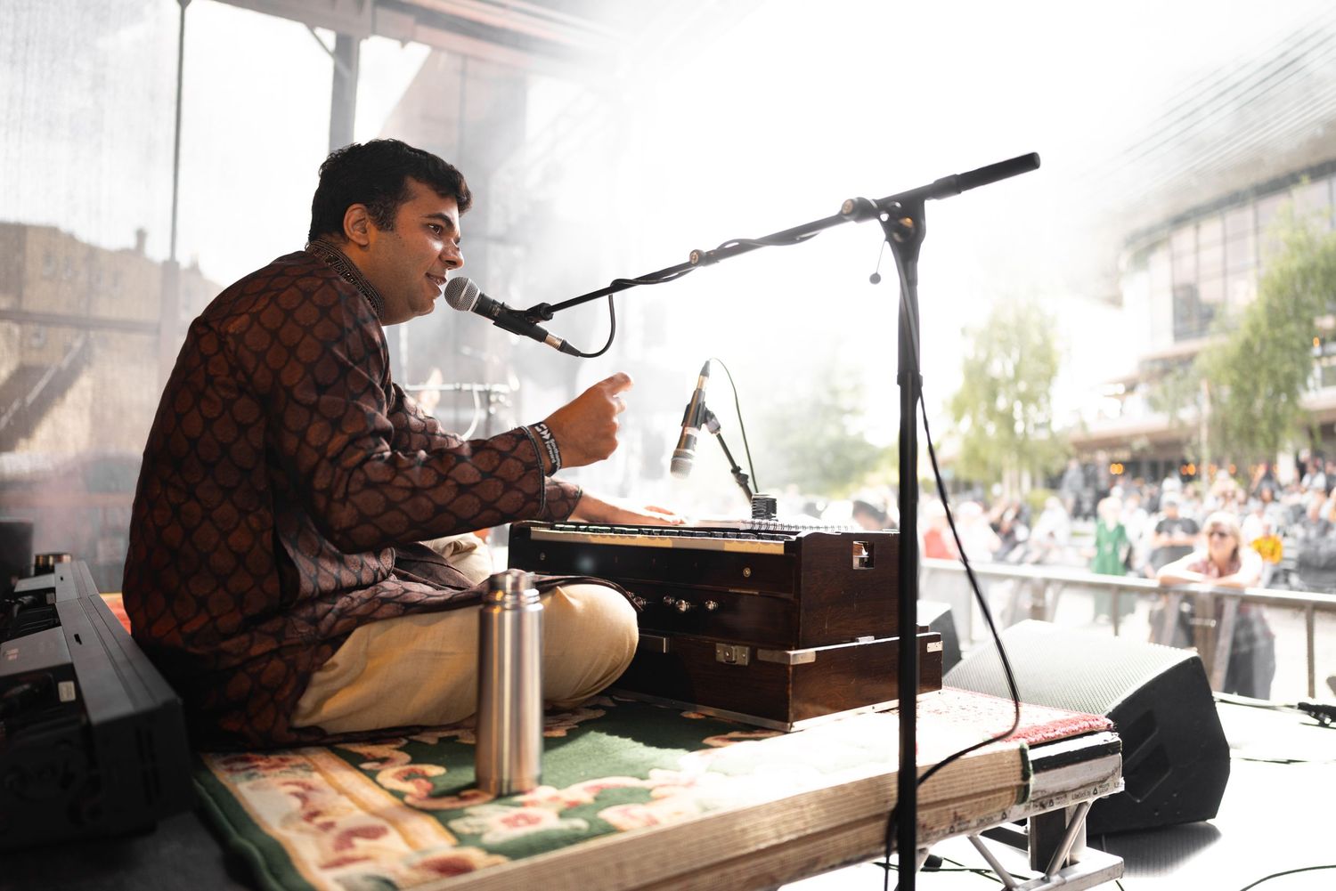 Musician seated cross-legged playing harmonium and singing at Tapestry festival with natural backlight, live music event photography