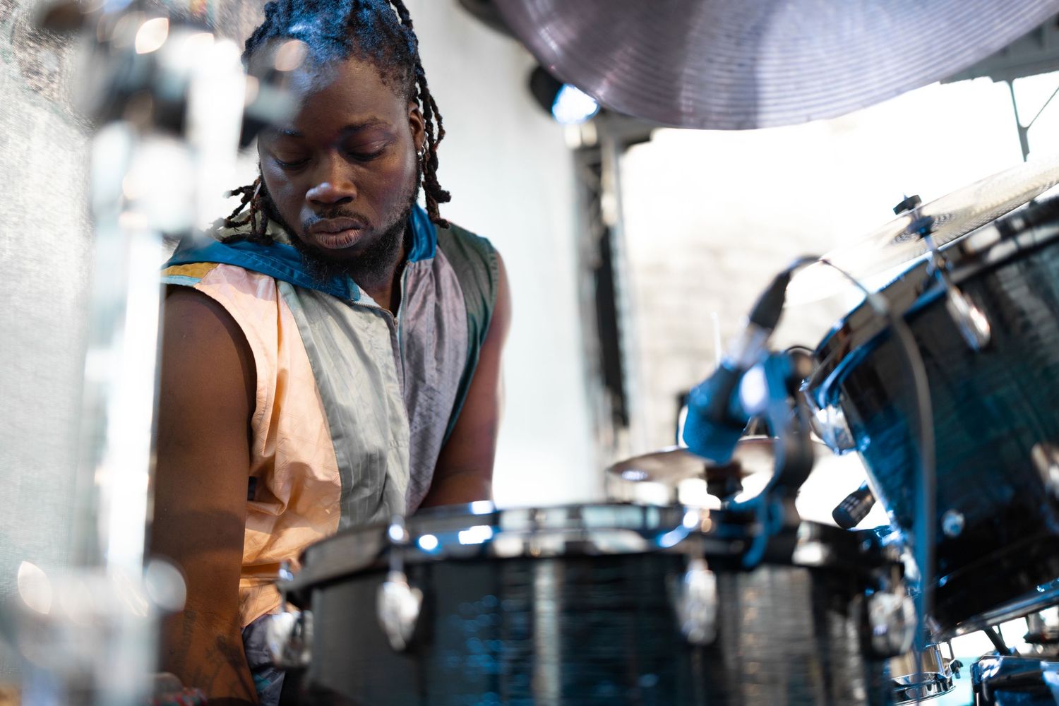 Drummer with locs playing a drum kit at Tapestry festival in a colourful vest, live music festival photography