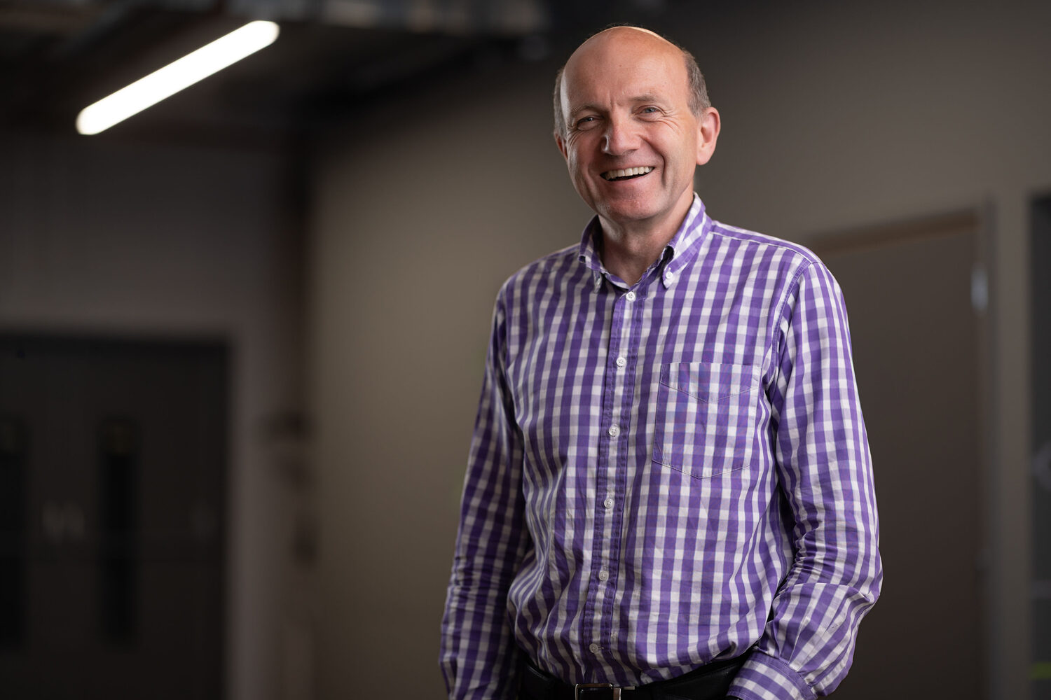 Board director in a purple check shirt smiling in a modern office corridor at Network Eagle Lab Southampton, corporate headshot photography for Go! Southampton BID