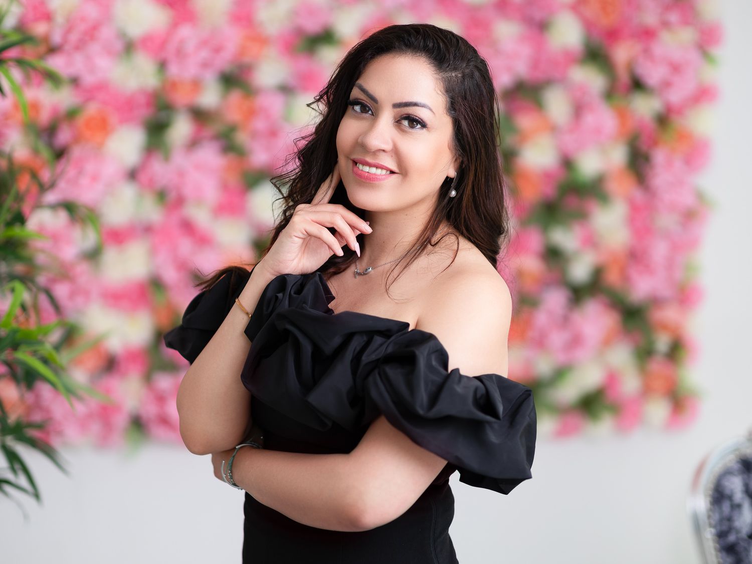 Leilah smiling in a black off-shoulder ruffled top with pink flower wall behind her, glamorous portrait photography Southampton