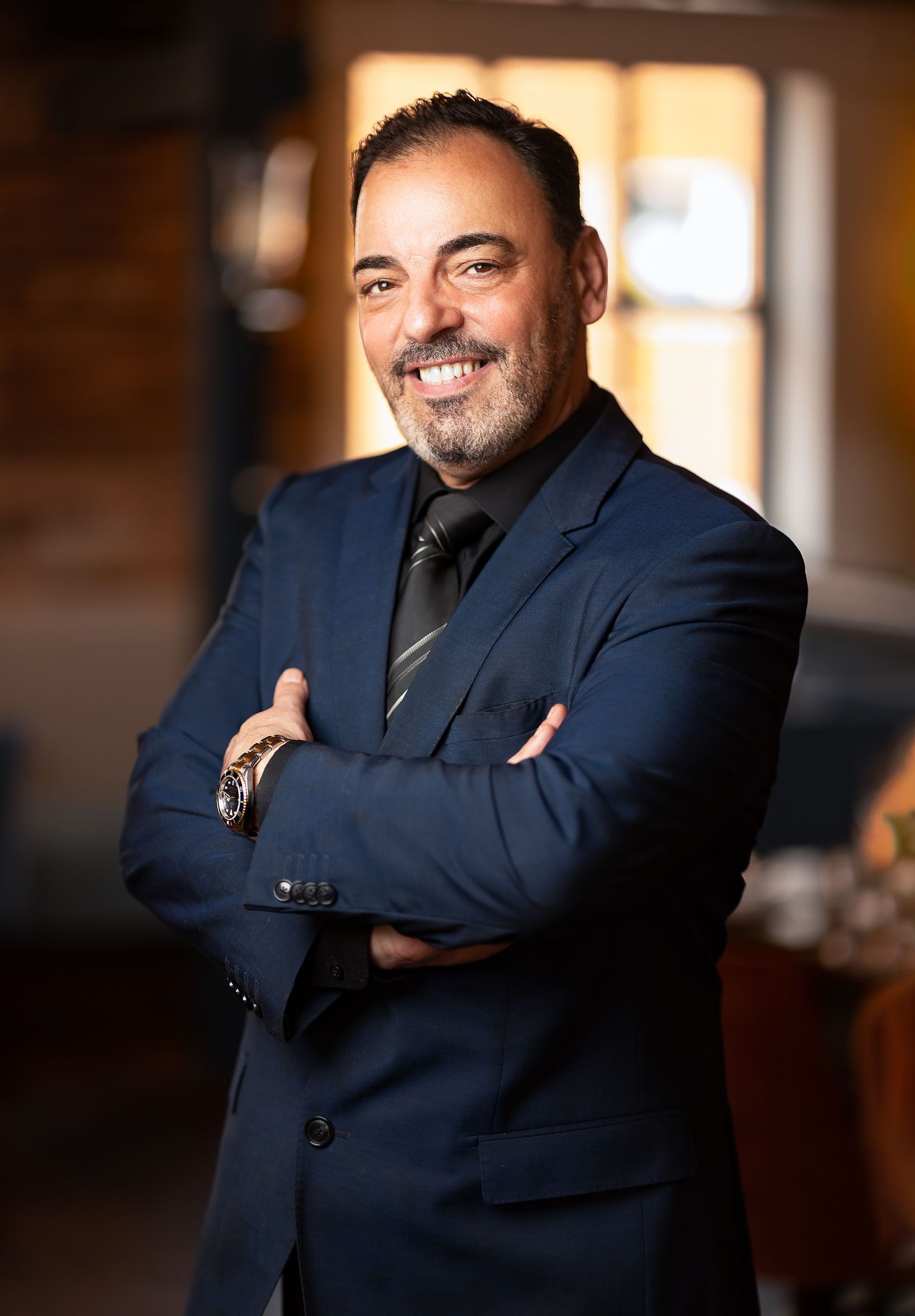 Smiling man in a navy suit and striped tie with arms crossed at Ocean Grill restaurant, hospitality business portrait photography Southampton