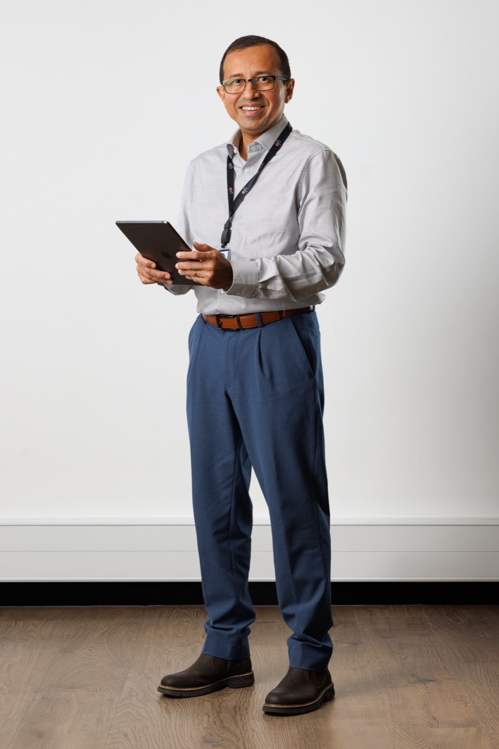 Smiling man in glasses standing full length with a tablet and lanyard against a white wall, corporate staff portrait for a company intranet and website banner, Southampton, corporate photography