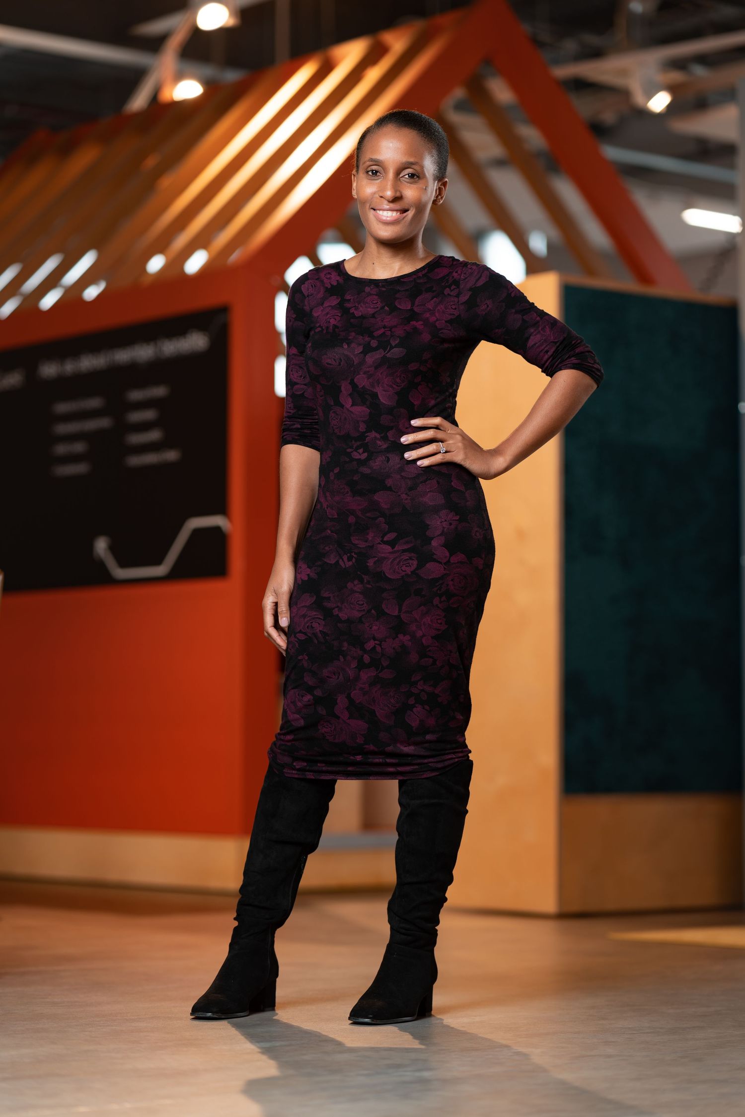 Woman in a dark floral dress and knee-high black boots standing confidently in a colourful modern workspace, full-length personal branding portrait photography Southampton