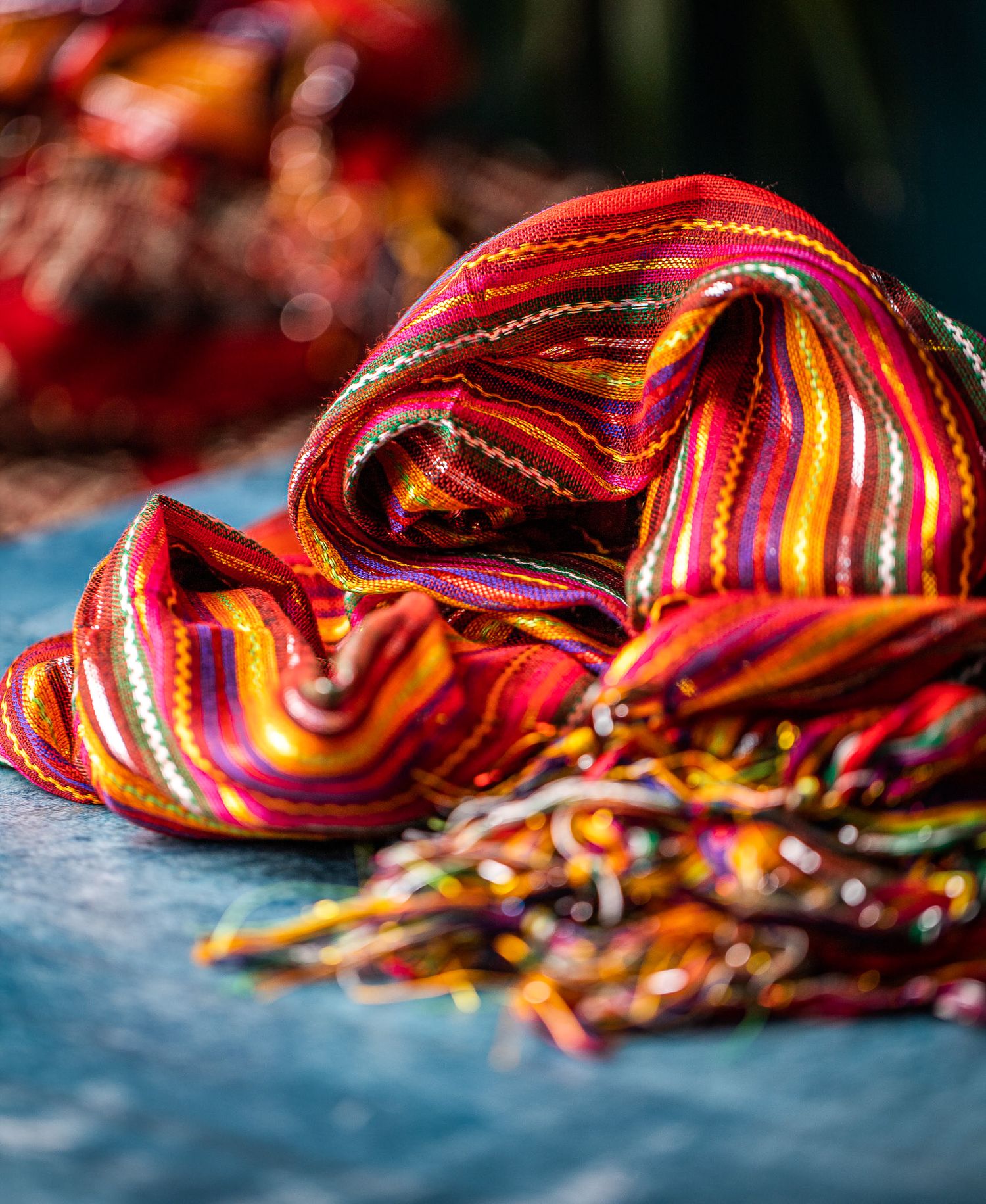Colourful handwoven scarf with red, pink and multicoloured stripes and tassels on a dark surface, textile product photography Southampton