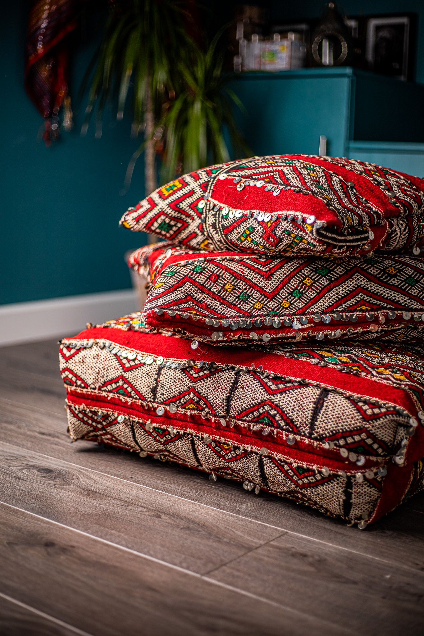 Stack of red and cream Moroccan-style embroidered floor cushions on a wooden floor with teal wall behind, homeware product photography Southampton