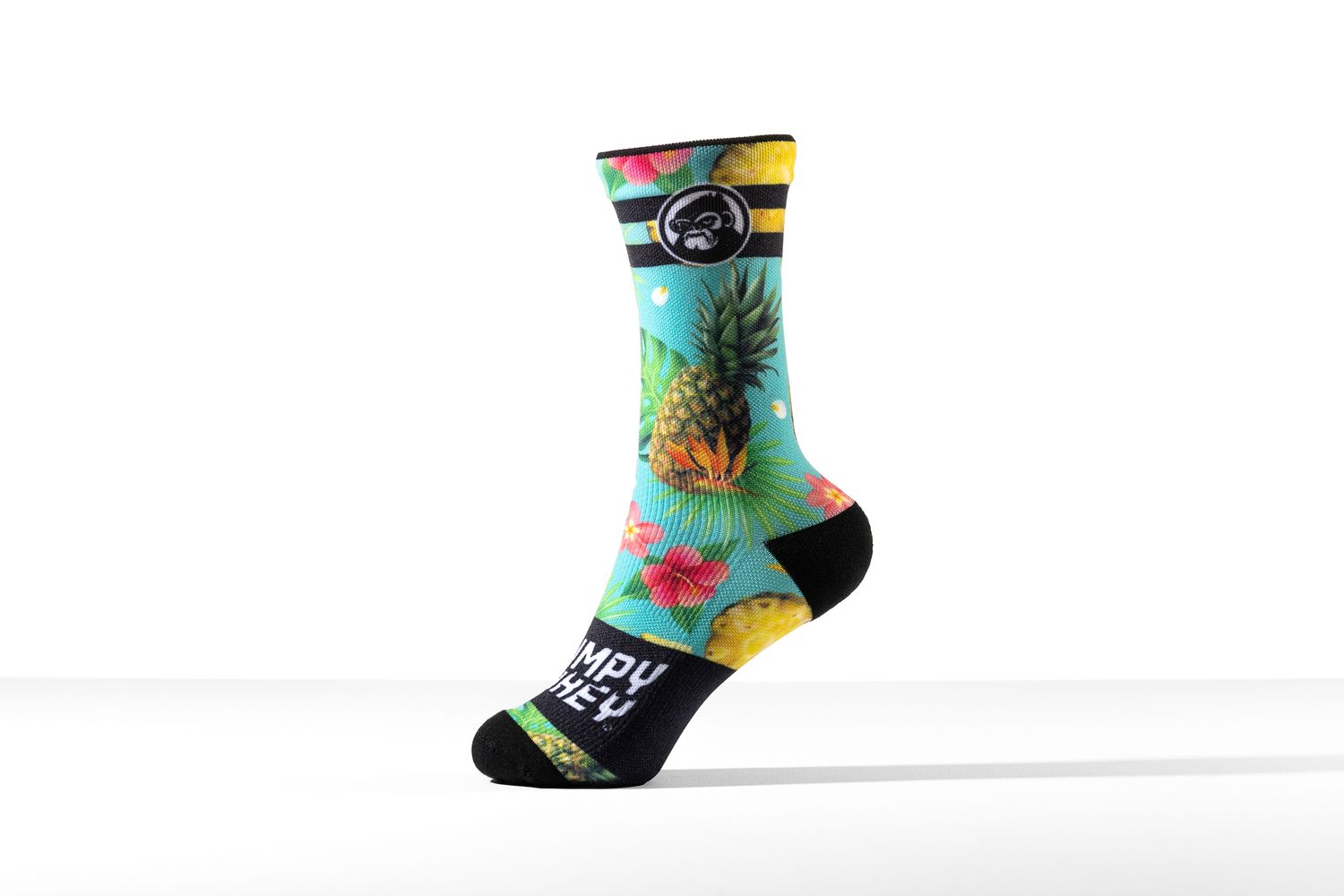 Single tropical-print sock with pineapple and floral pattern standing upright on a white background for Grumpy Monkey, apparel product photography