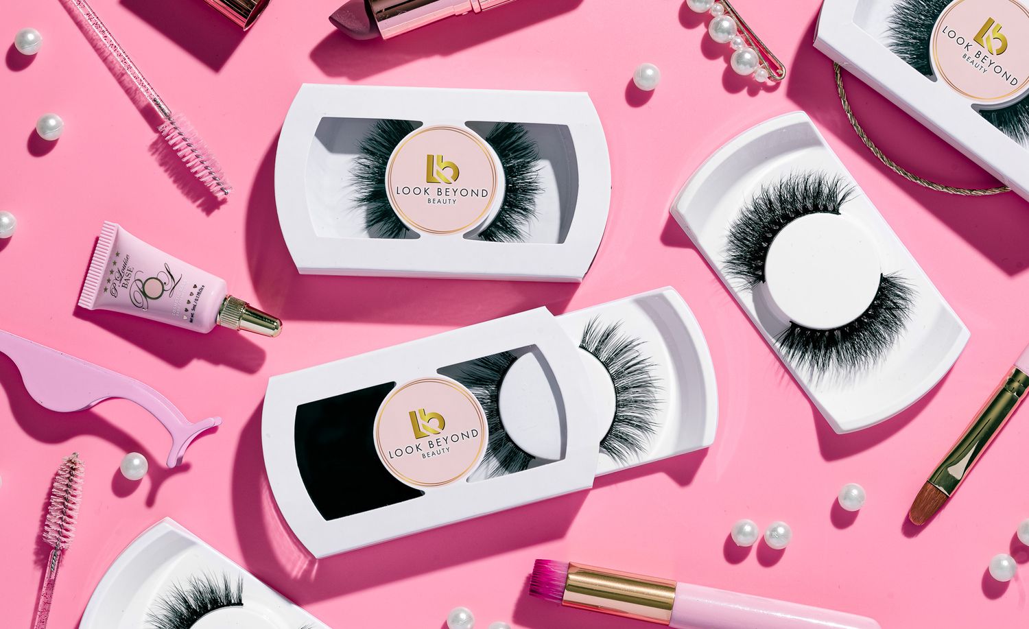 Multiple Look Beyond Beauty false eyelash sets in branded packaging with beauty accessories on a pink background, cosmetics product photography