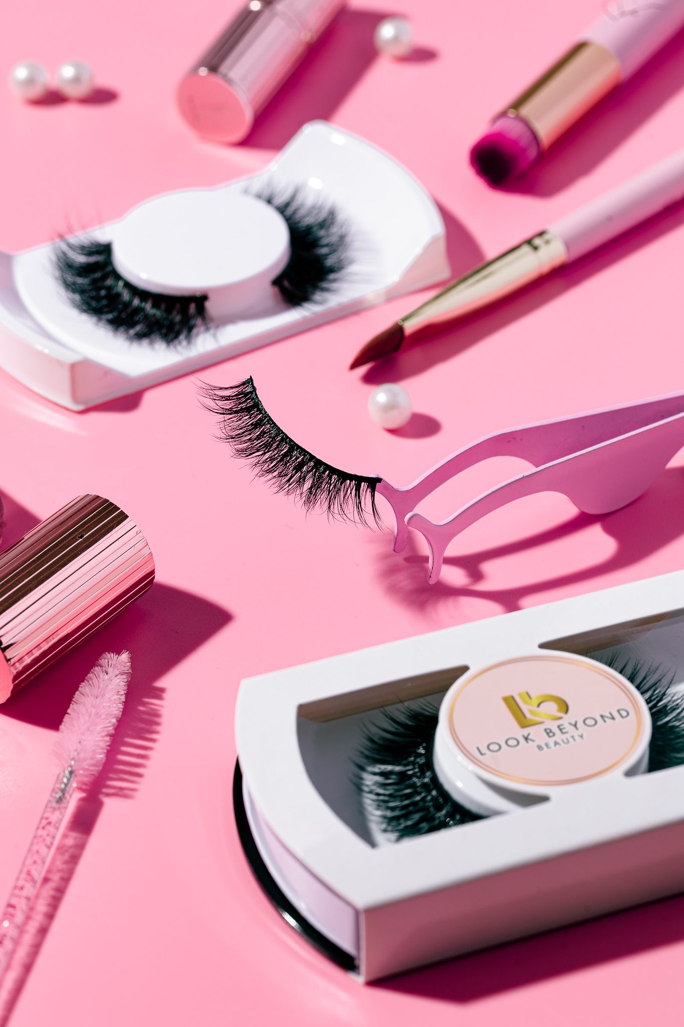 False eyelashes, lash applicator, lipstick and beauty accessories on a pink background for Look Beyond Beauty, cosmetics product photography