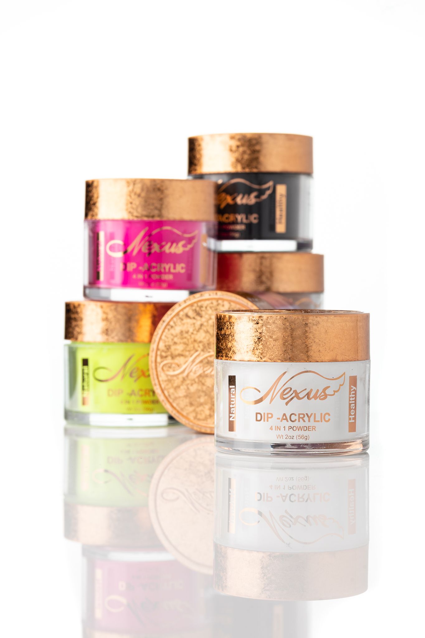 Nexus dip-acrylic nail powder jars in multiple colours with rose gold lids on a reflective white surface, beauty product photography Southampton