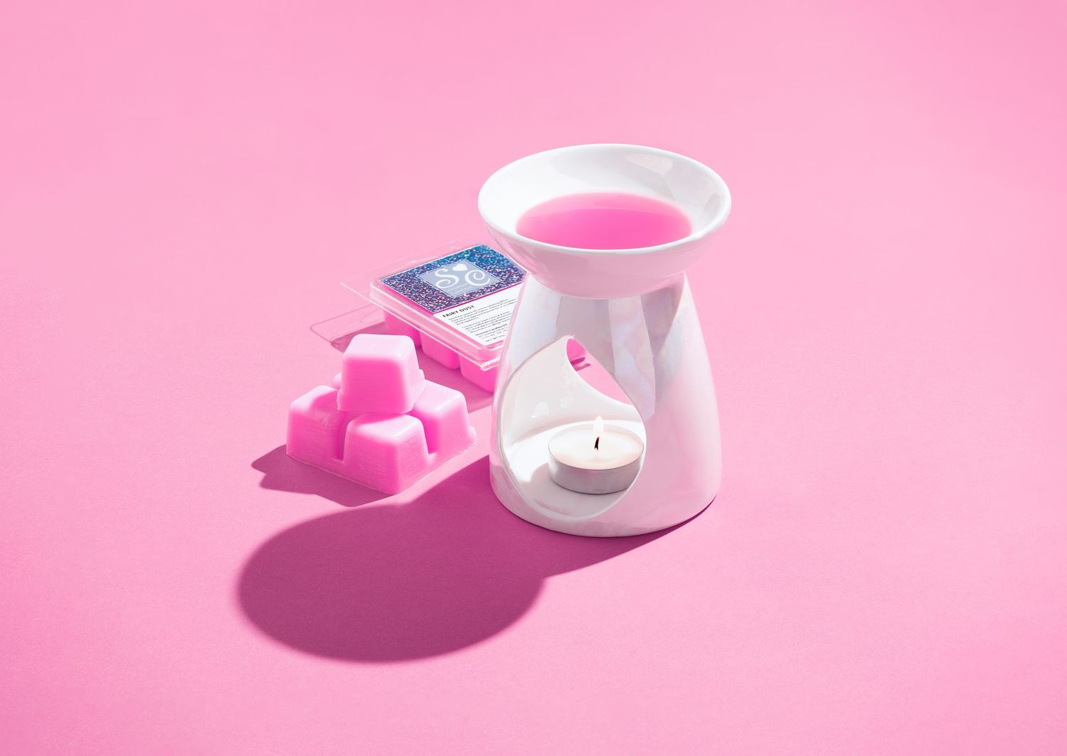 Pink wax melt burner with melted wax, pink wax melt cubes and branded packaging on a pink background, home fragrance product photography Southampton