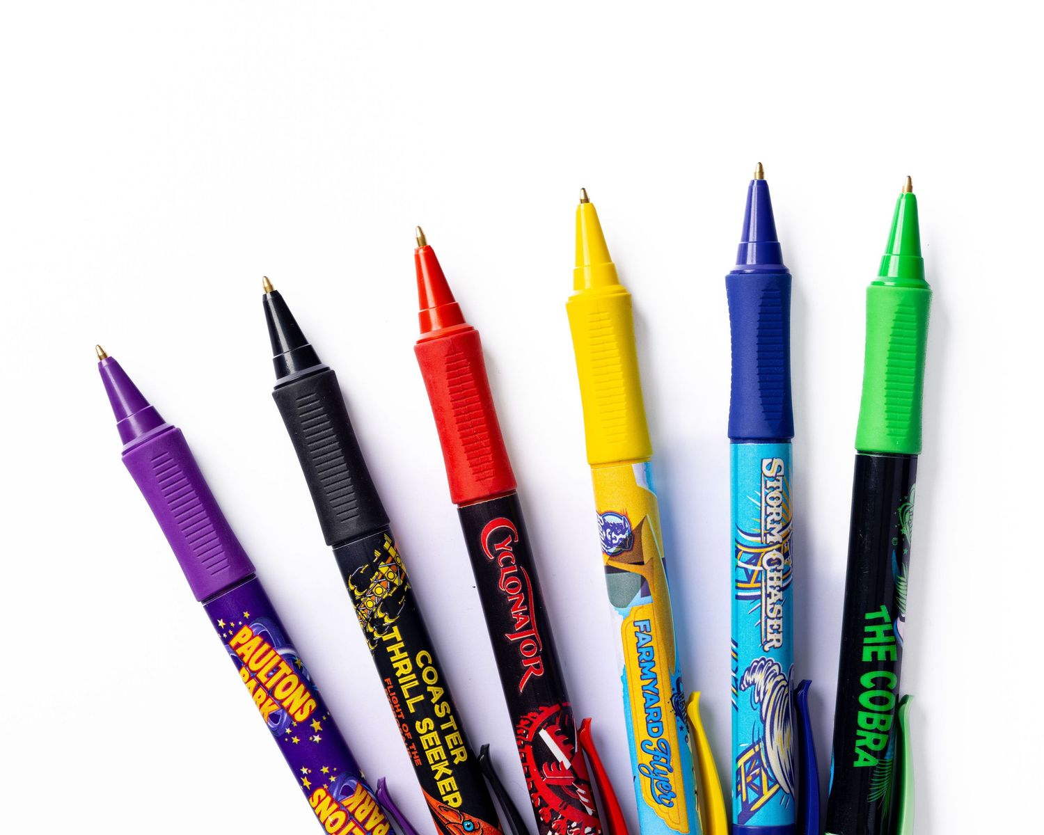 Colourful branded ballpoint pens with ride names fanned out on a white background for Paultons Park, stationery merchandise product photography