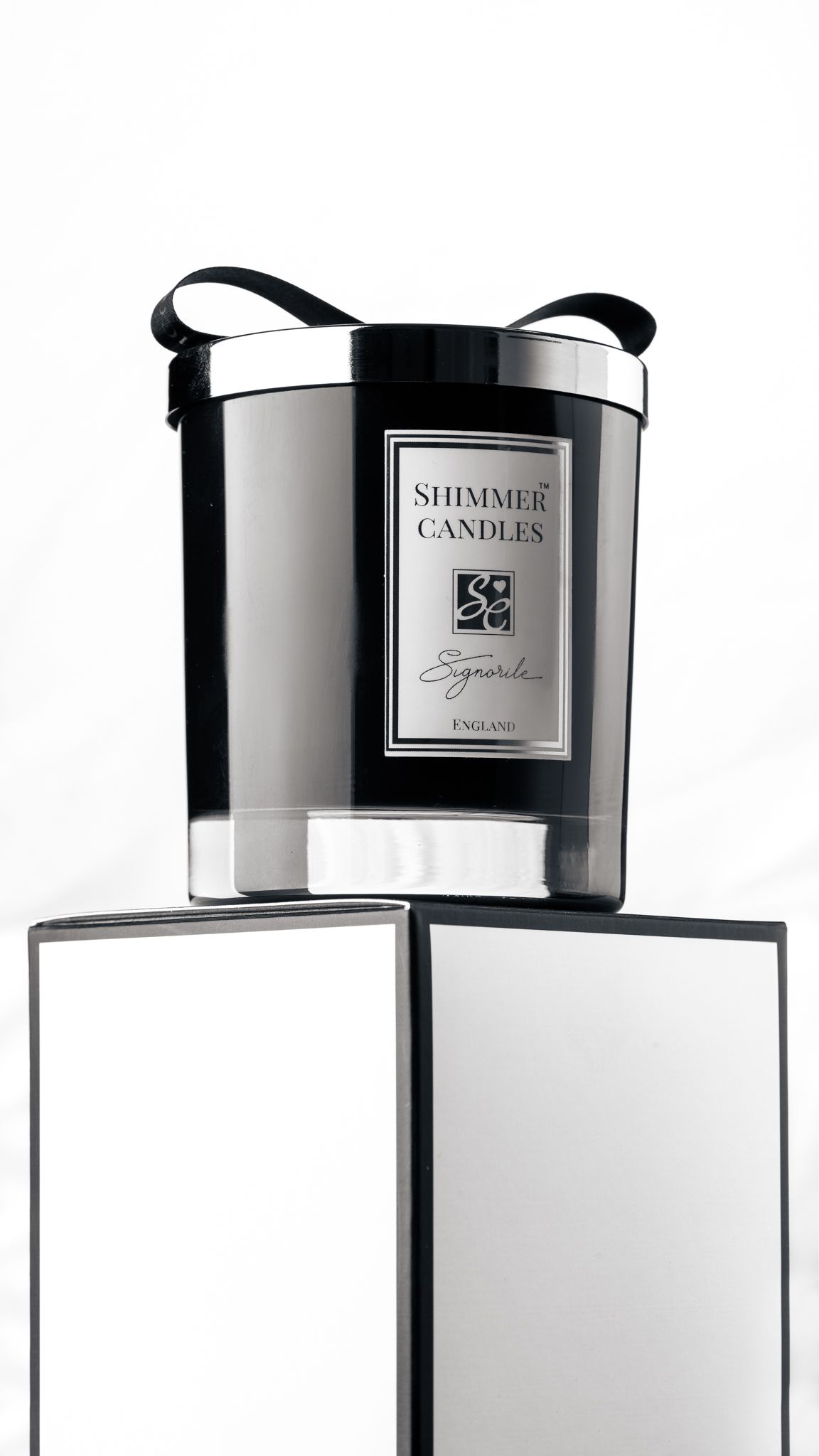 Shimmer Candles Signorile luxury black candle with silver label on a mirrored plinth against a white background, premium product photography Southampton