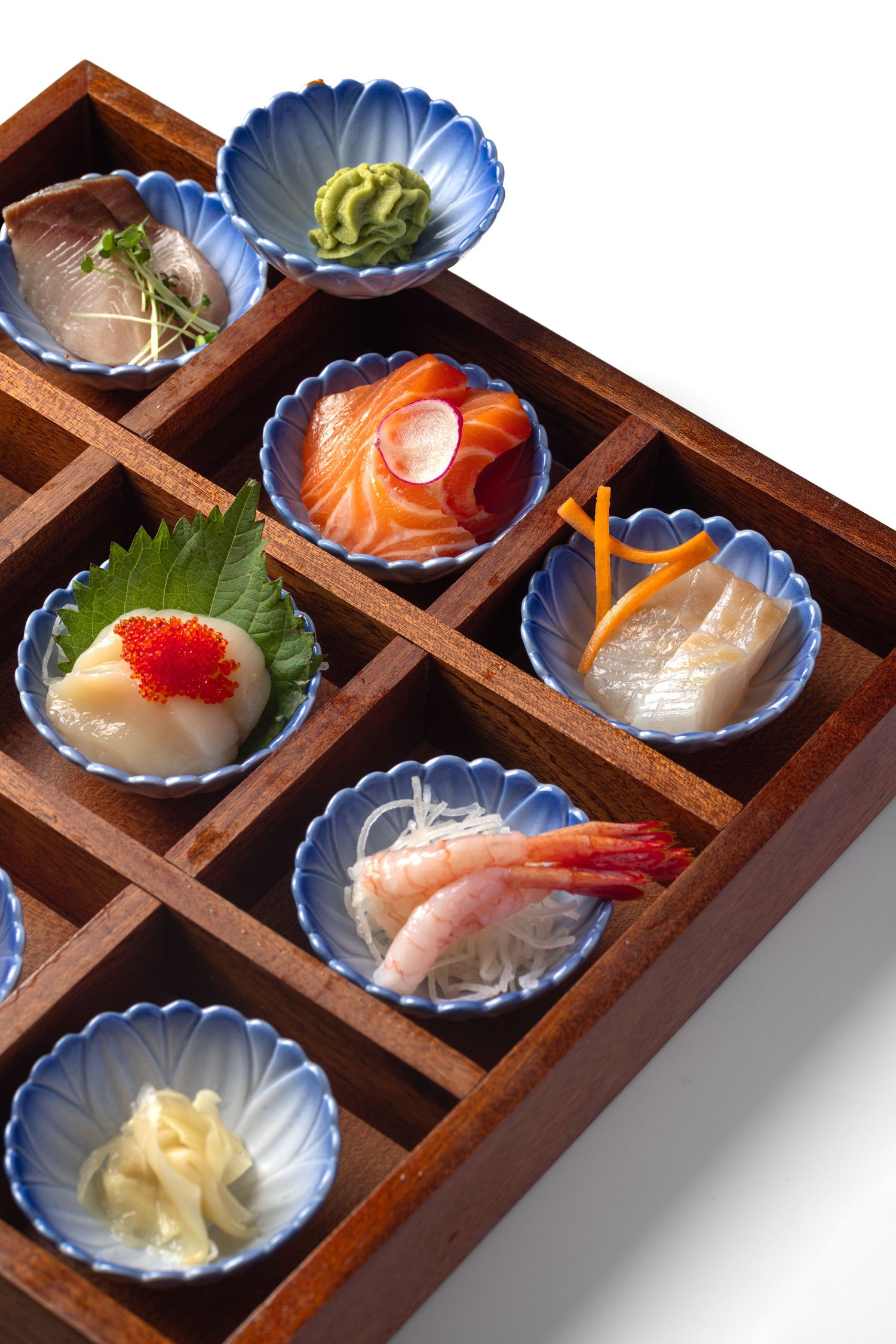 Japanese sashimi selection with salmon, prawns and wasabi in blue scalloped dishes in a wooden compartment box for Roppongi restaurant, food product photography