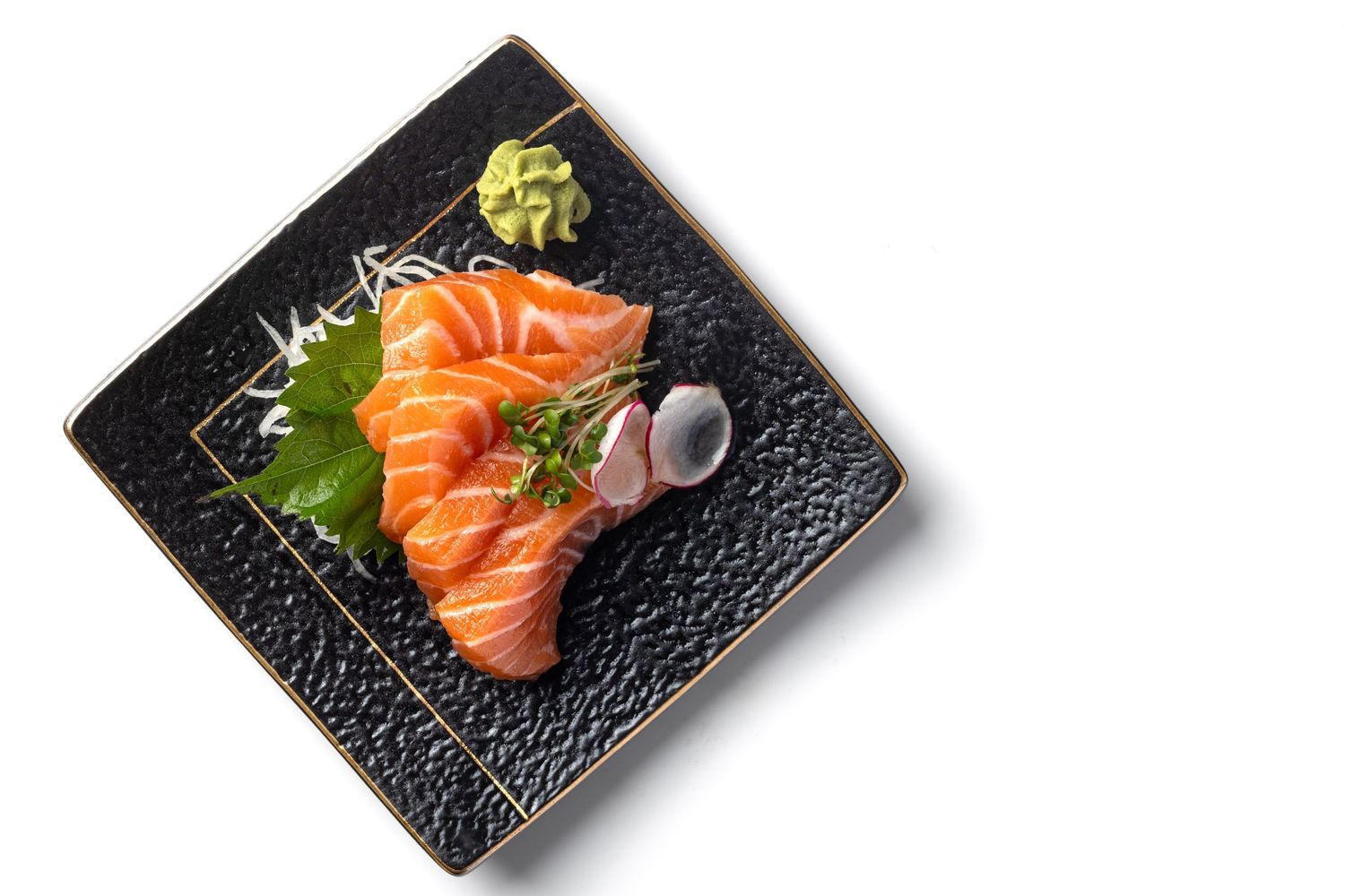 Salmon sashimi with wasabi, shiso leaf and microgreens on a black textured plate on a white surface for Roppongi restaurant, food styling product photography