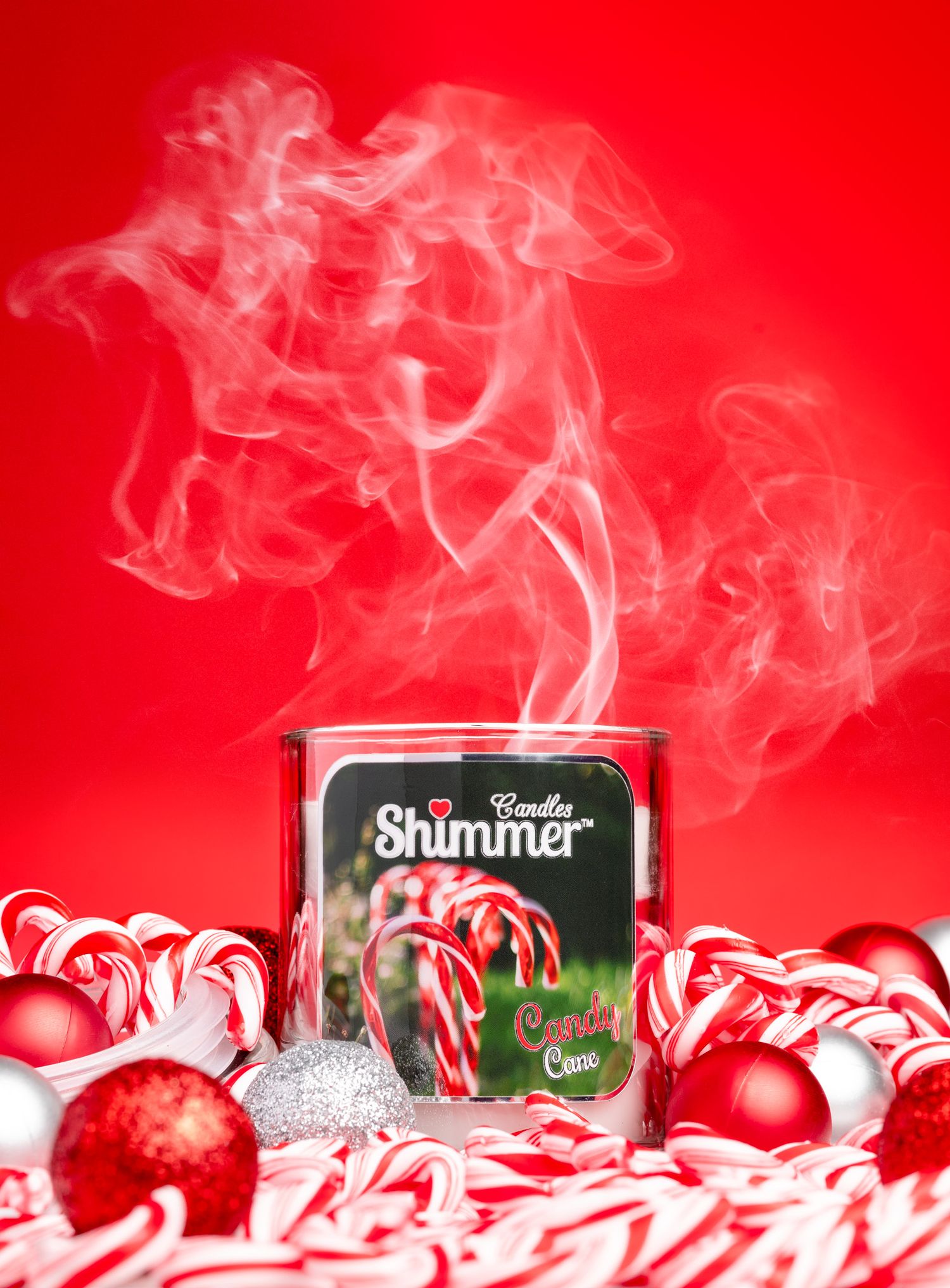 Shimmer Candles candy cane scented candle with smoke rising surrounded by candy canes and red baubles on a red background, festive product photography Southampton