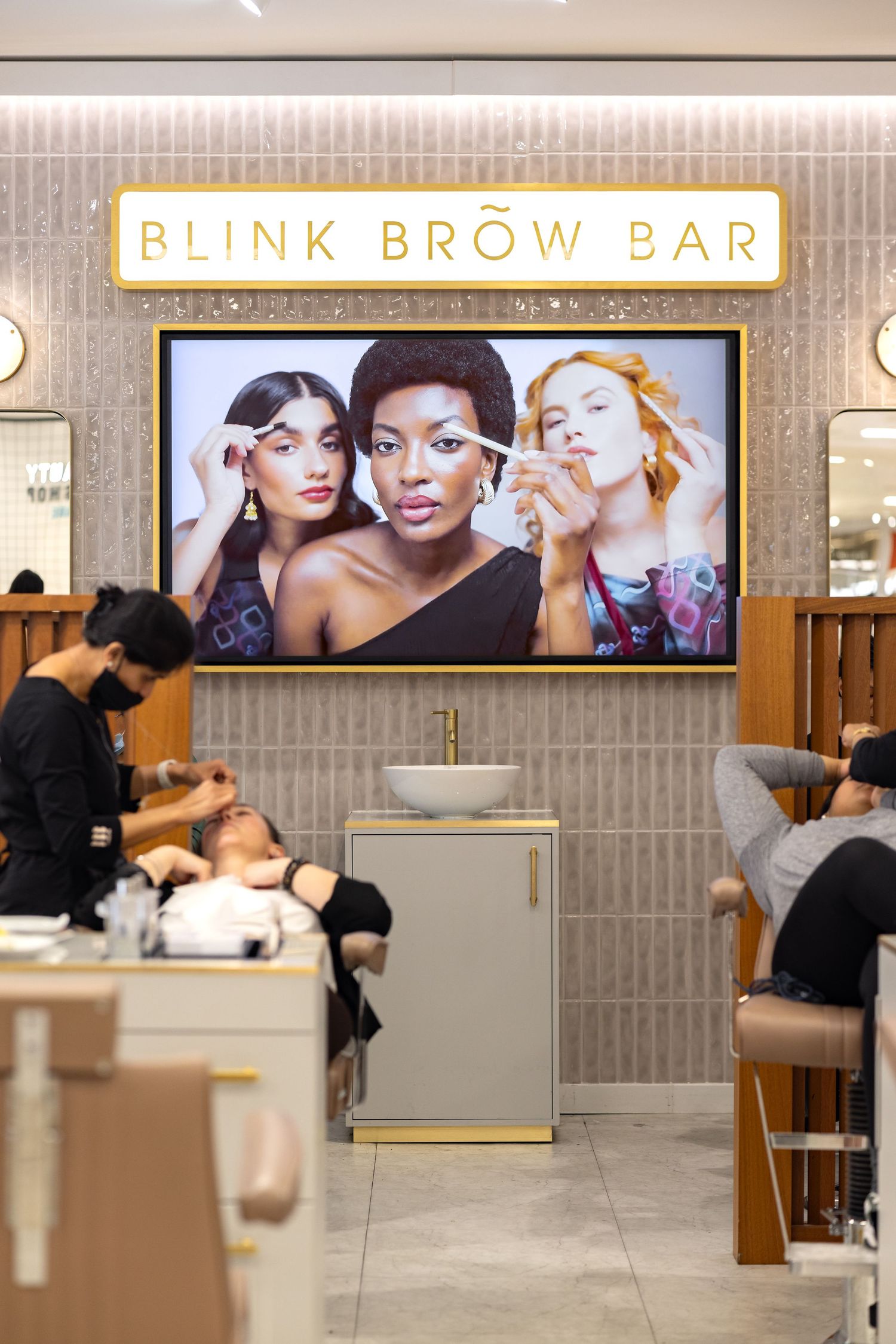 TrouDigital large digital screen at Blink Brow Bar showing beauty imagery with customers being treated below, digital signage product photography
