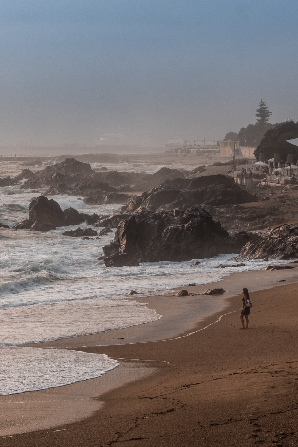 Hazy beach and rocky shoreline with a lone figure at the water's edge, Foz do Douro, Porto, Portugal, travel photography