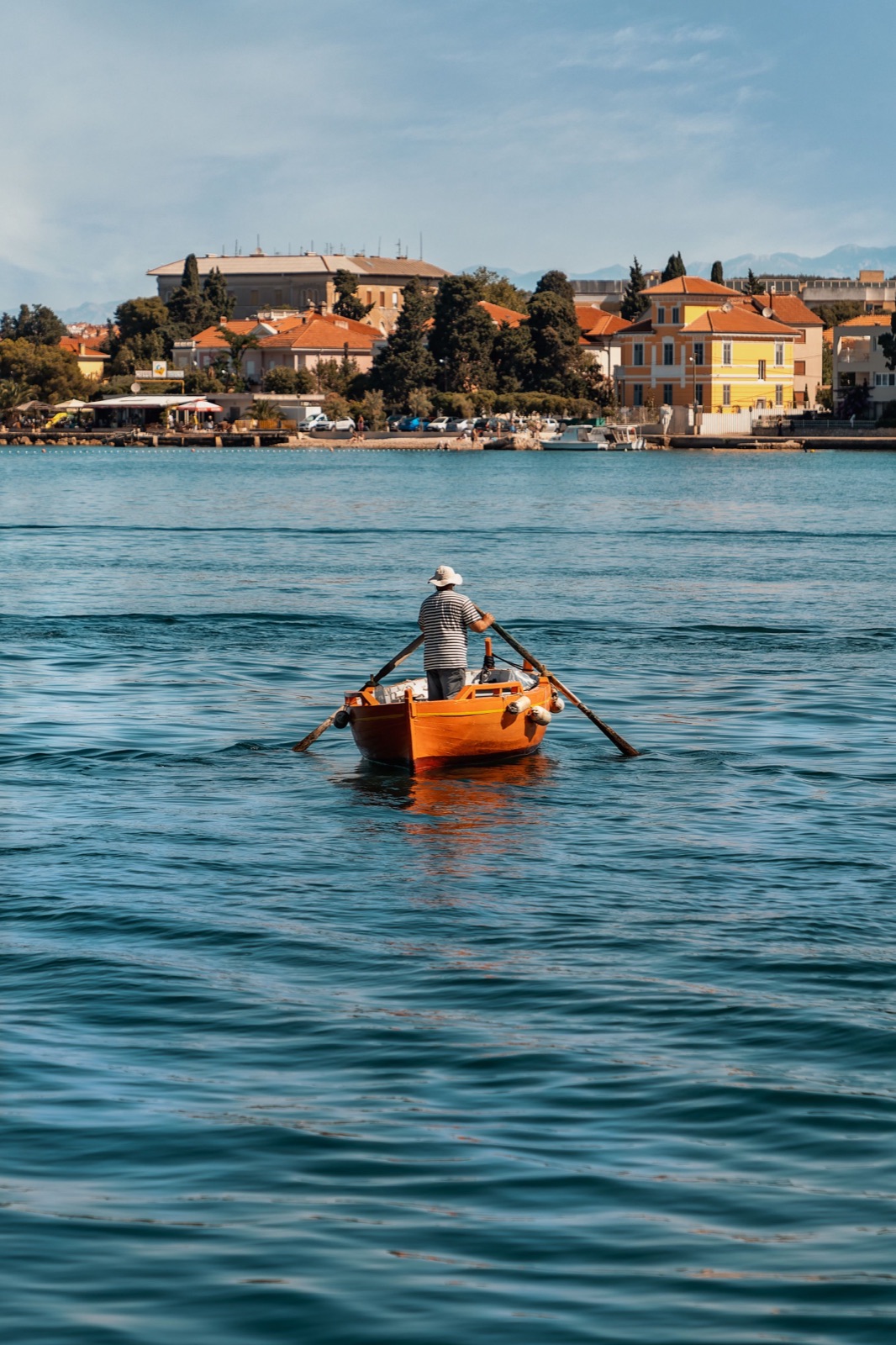 A man rowing a small orange boat across the bay, Zadar, Croatia, travel photography