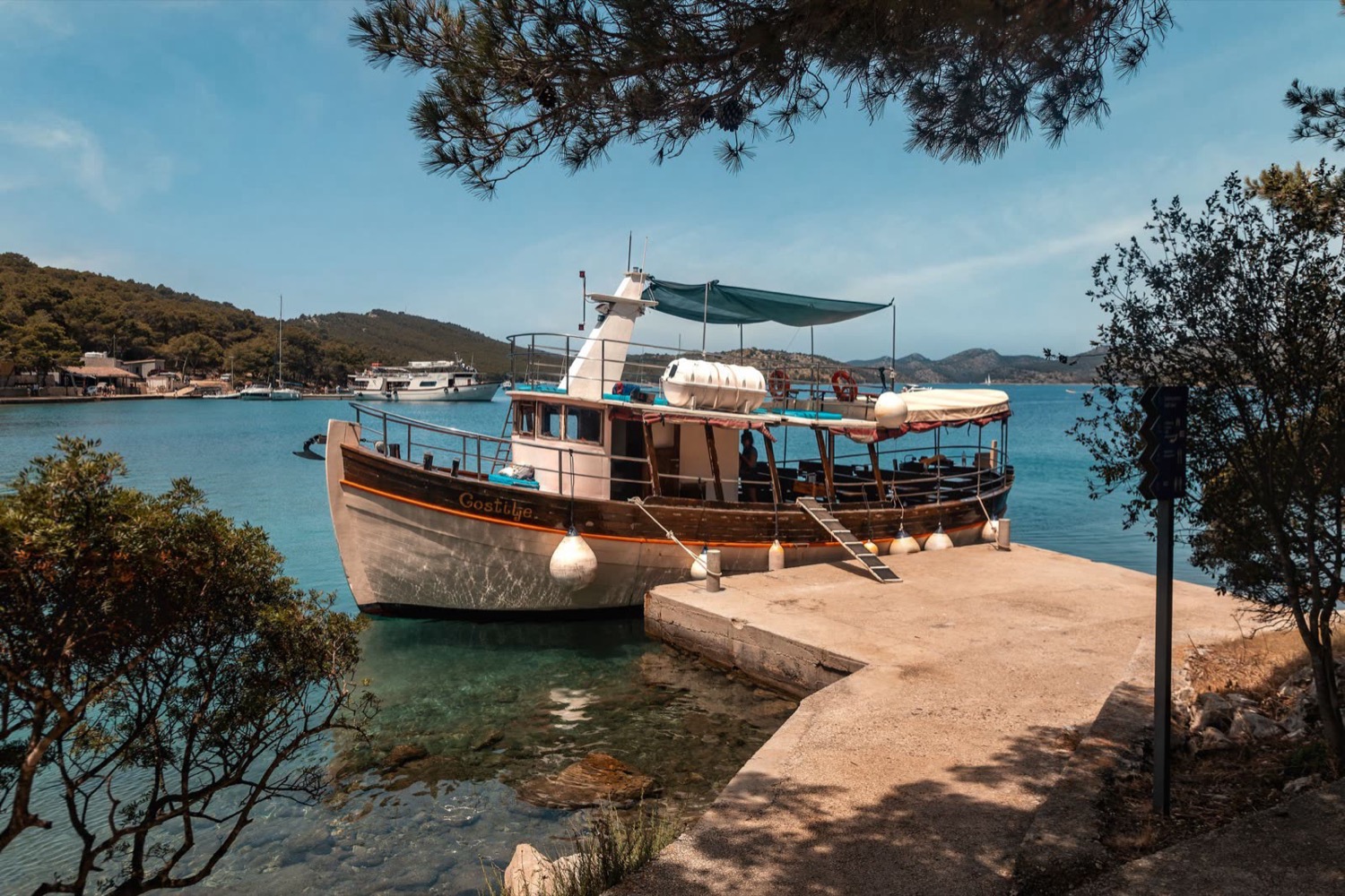 Wooden boat moored at a stone jetty beneath pine trees, Zadar, Croatia, travel photography