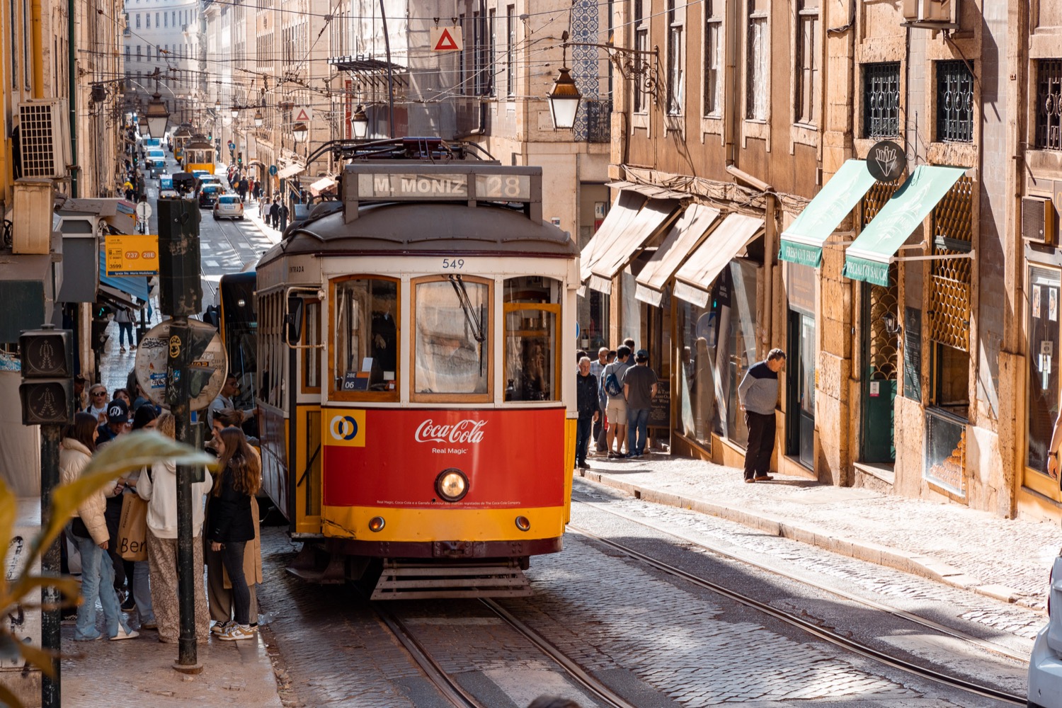 Yellow and red tram working up a narrow shopping street, Lisbon, Portugal, travel photography