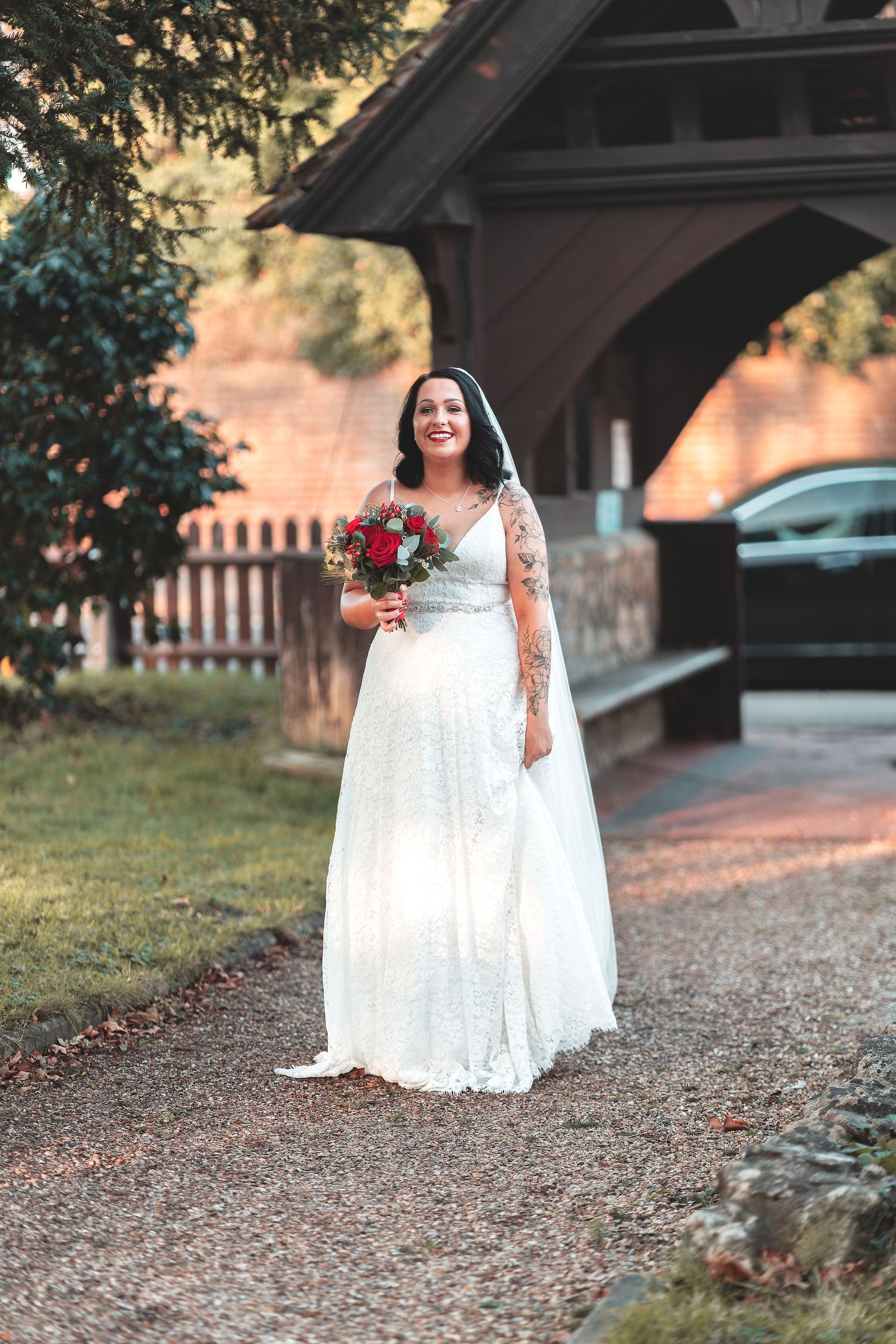 Tattooed bride in white lace dress and veil walking with bouquet near a wooden lychgate church entrance in Hamble, bridal arrival wedding photography Southampton