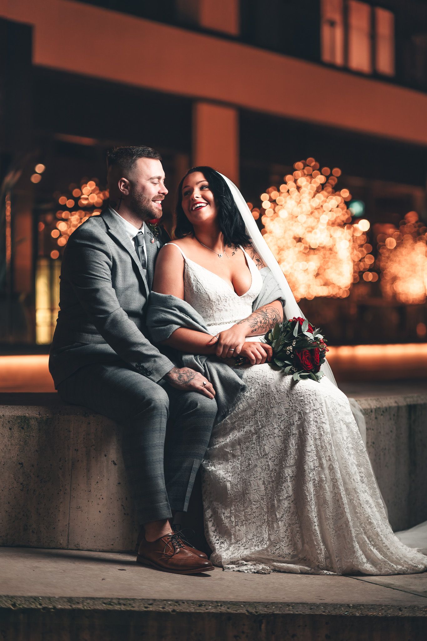 Bride and groom seated close together in the evening, framed by warm fairy-light bokeh outside the Harbour Hotel in Southampton, cinematic wedding photography