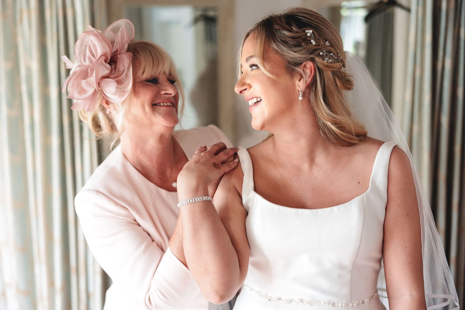 Bride sharing an emotional, happy moment with her mother during the morning preparations, the mother in a pink fascinator, candid wedding photography