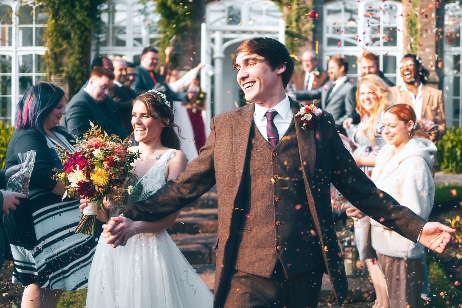 Bride and groom walking through confetti thrown by guests outside a venue, joyful wedding exit photography St Audrie\